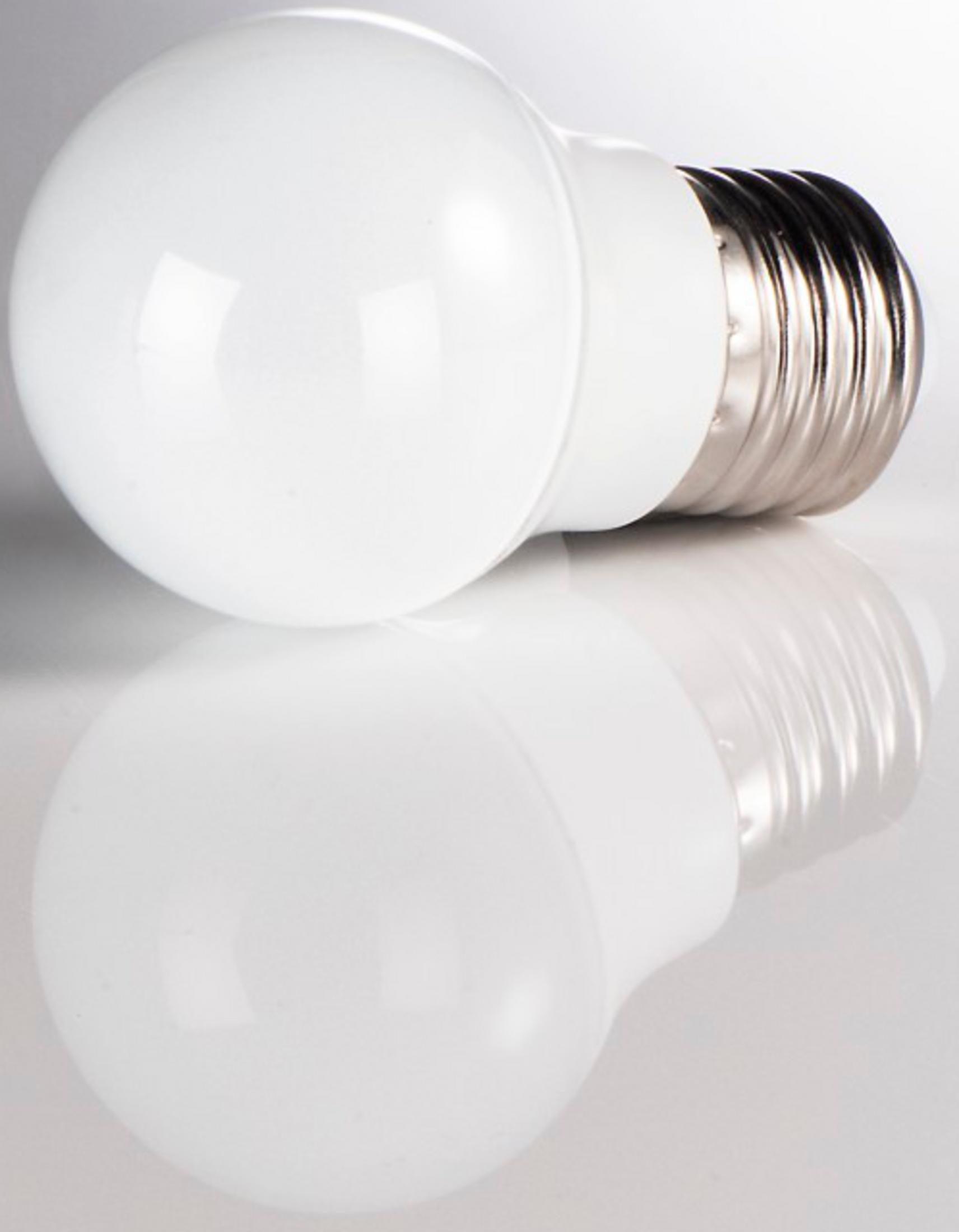 Una lampadina LED bianca con base in metallo poggia su una superficie riflettente.