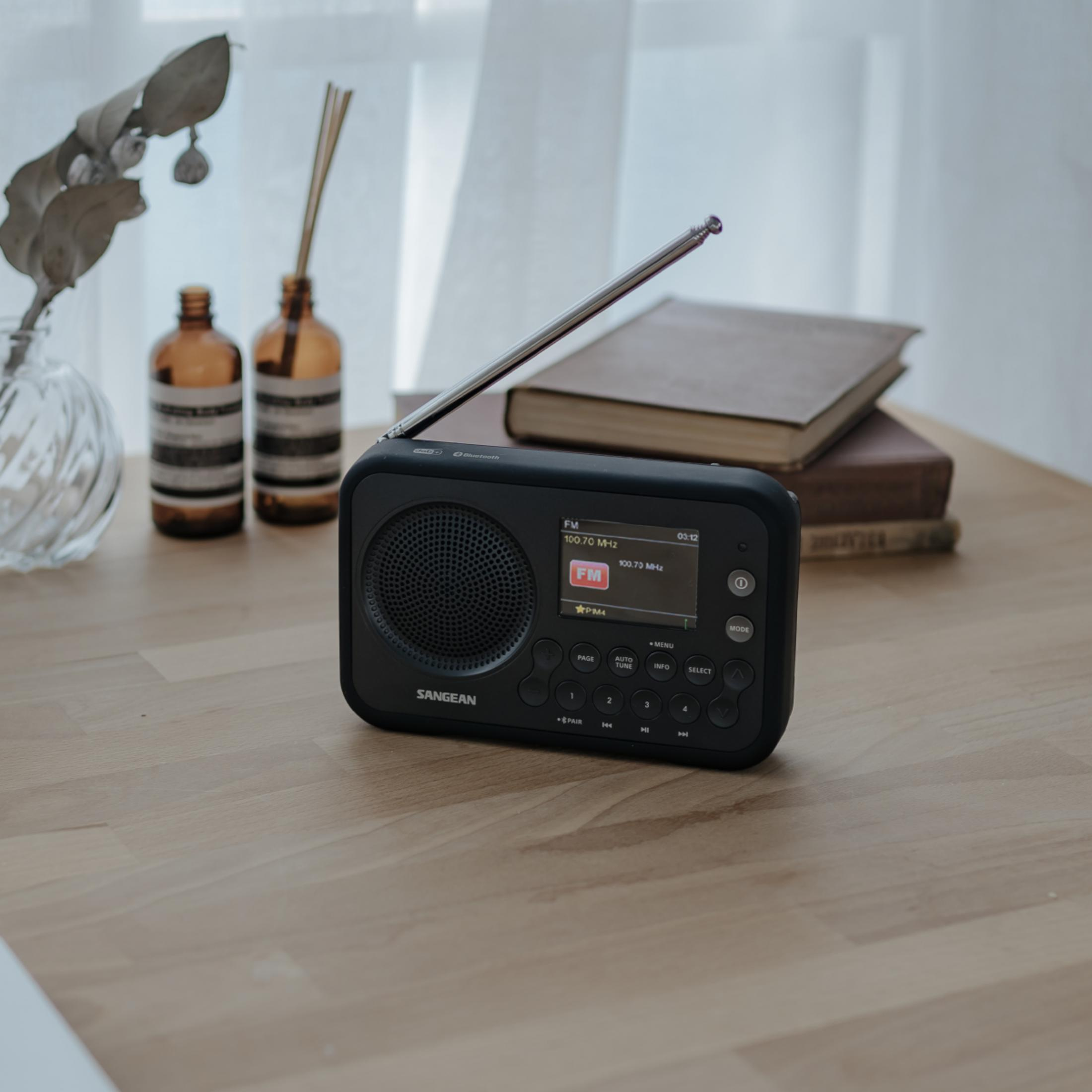 Une radio Sangean noire avec son antenne déployée, posée sur une table en bois.