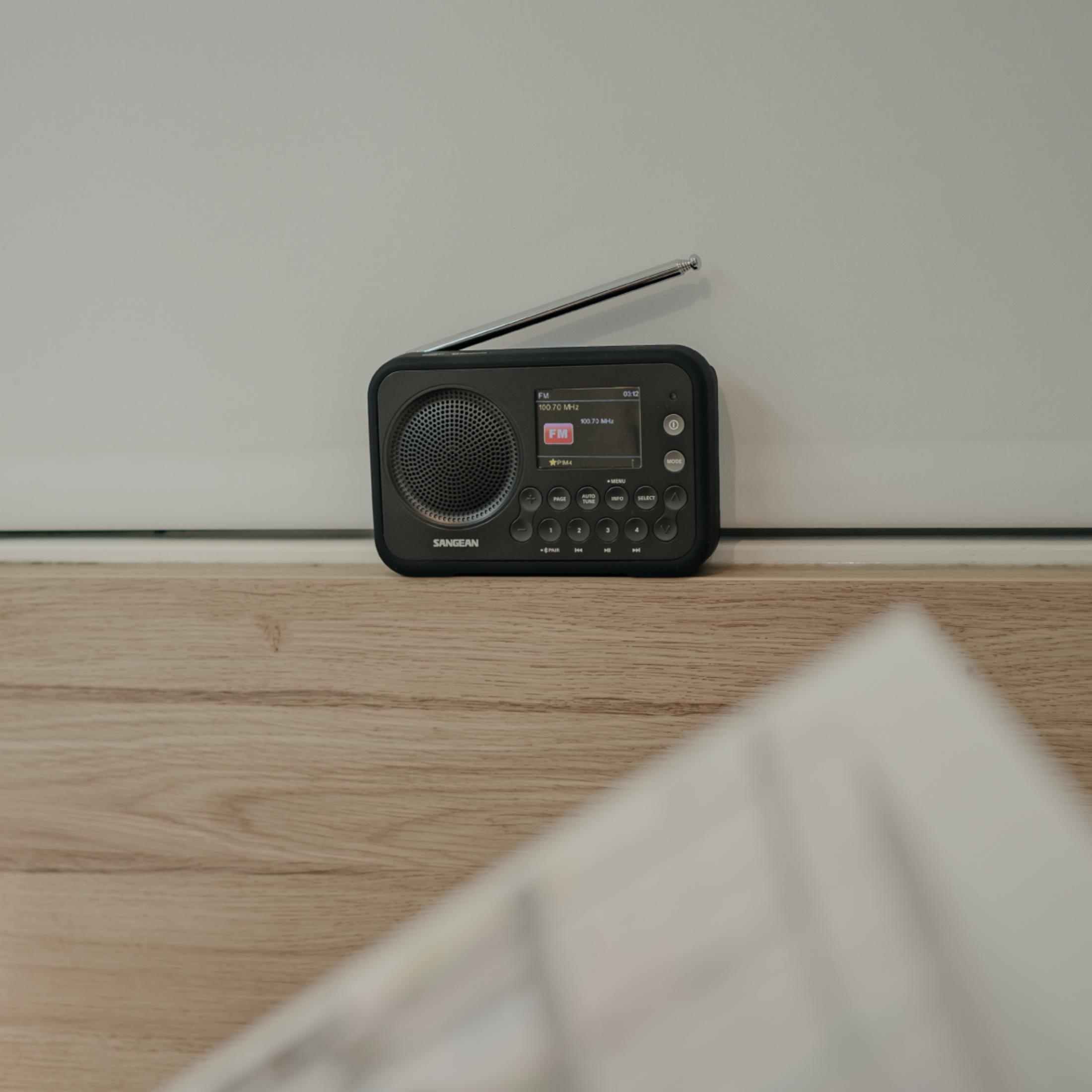 Une radio Sangean noire avec son antenne étendue, posée sur une surface en bois.