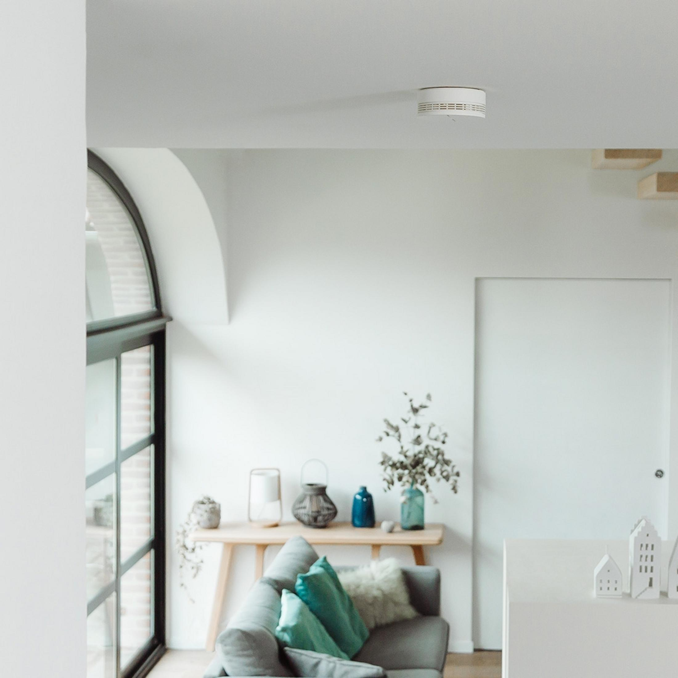 Smoke detector on the ceiling above a living room with sofa and console table.