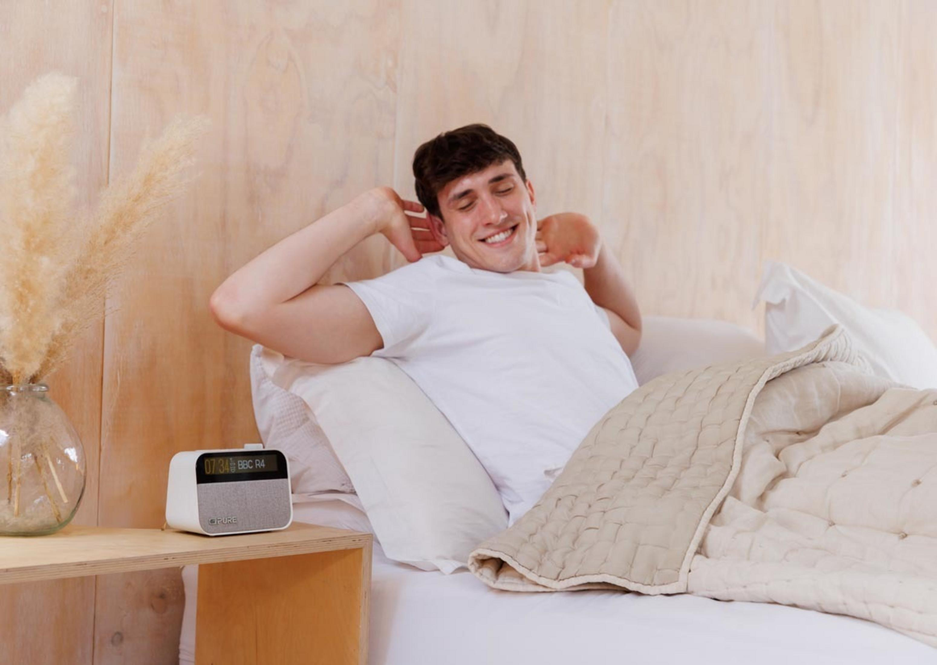 Un hombre se estira en la cama, una radio en la mesita de noche.