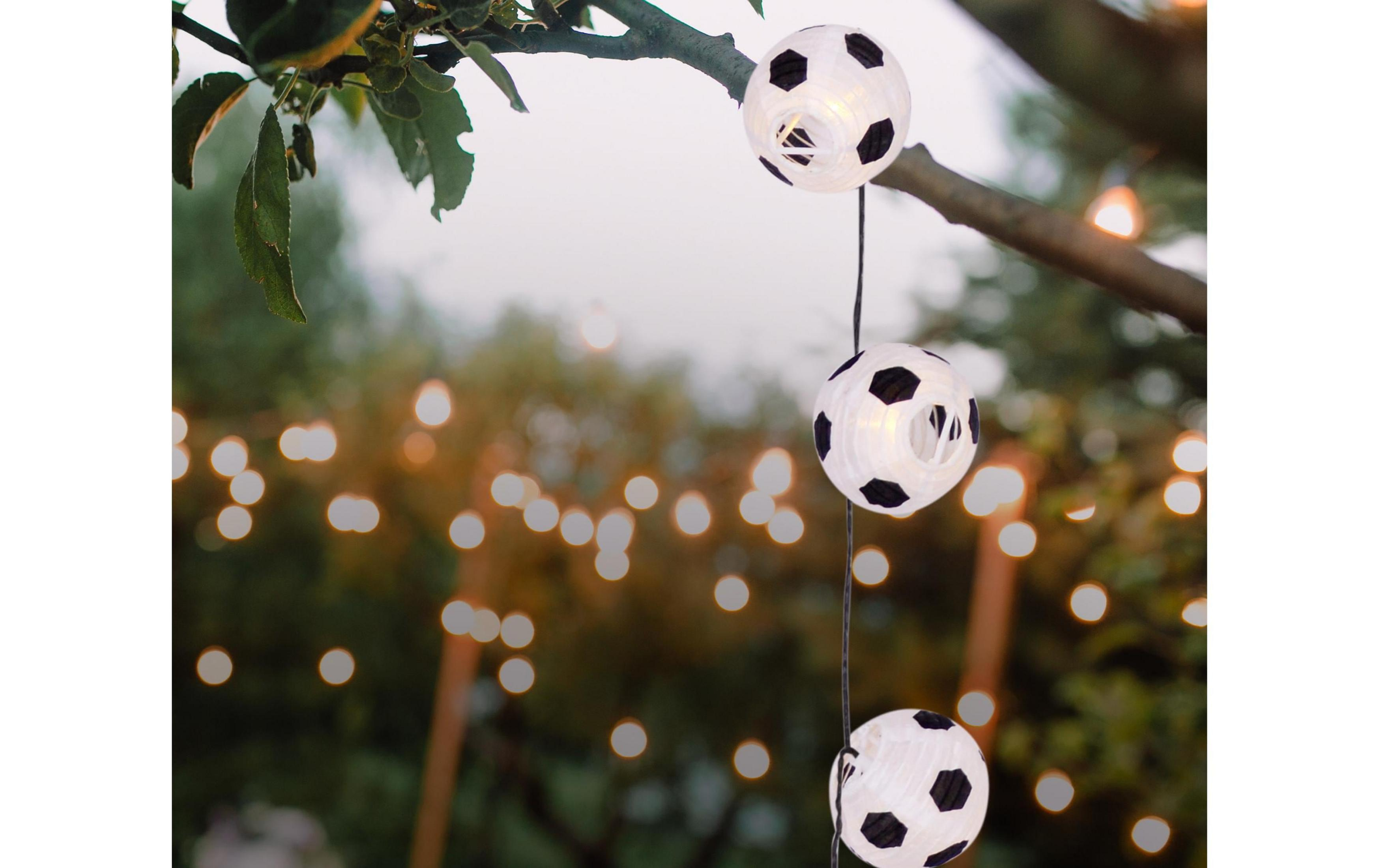 Drei weiße Lichterketten in Fußballform hängen an einem Ast.