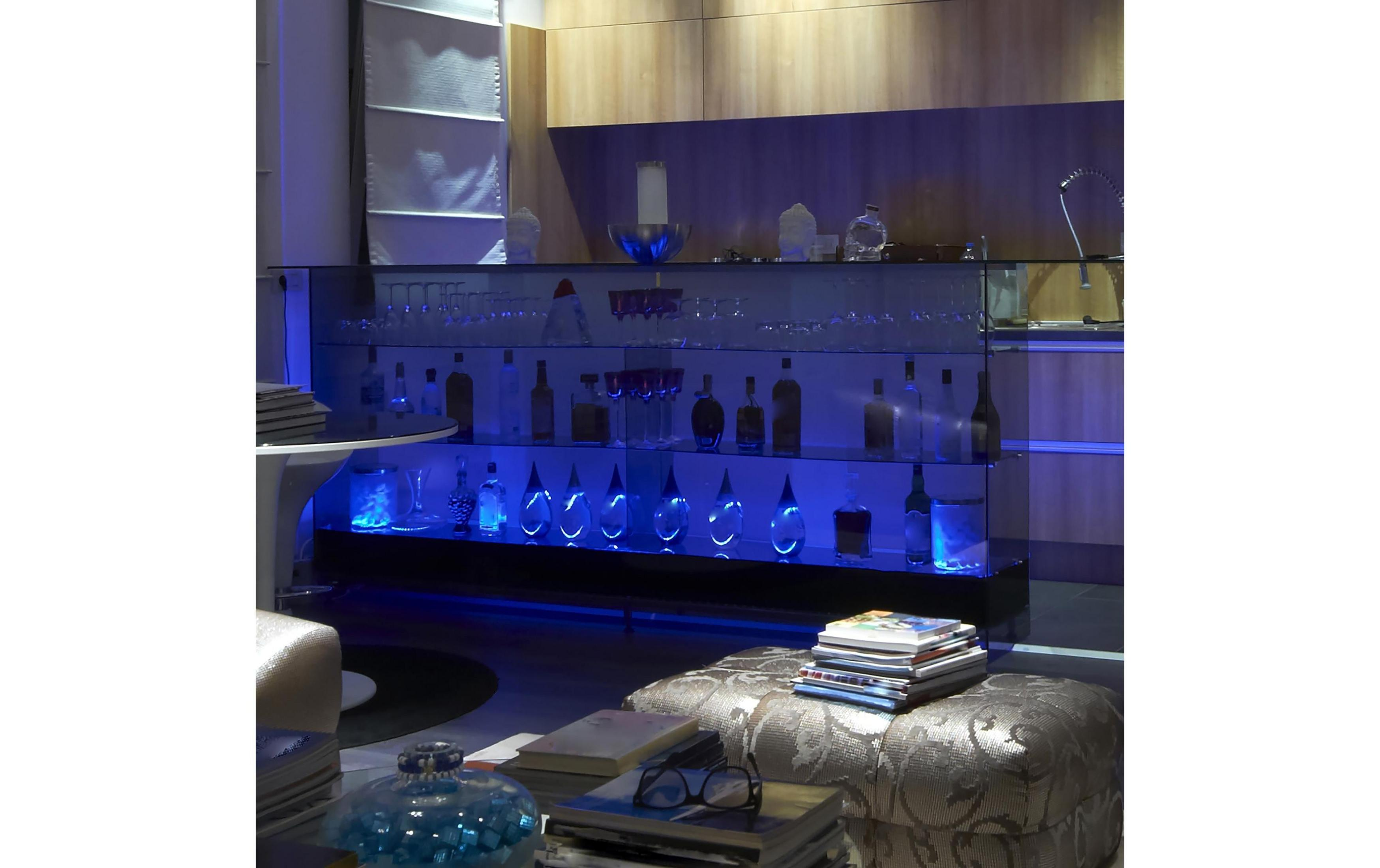 Eine Bar mit blau beleuchteten Regalen, gefüllt mit Flaschen und Gläsern.