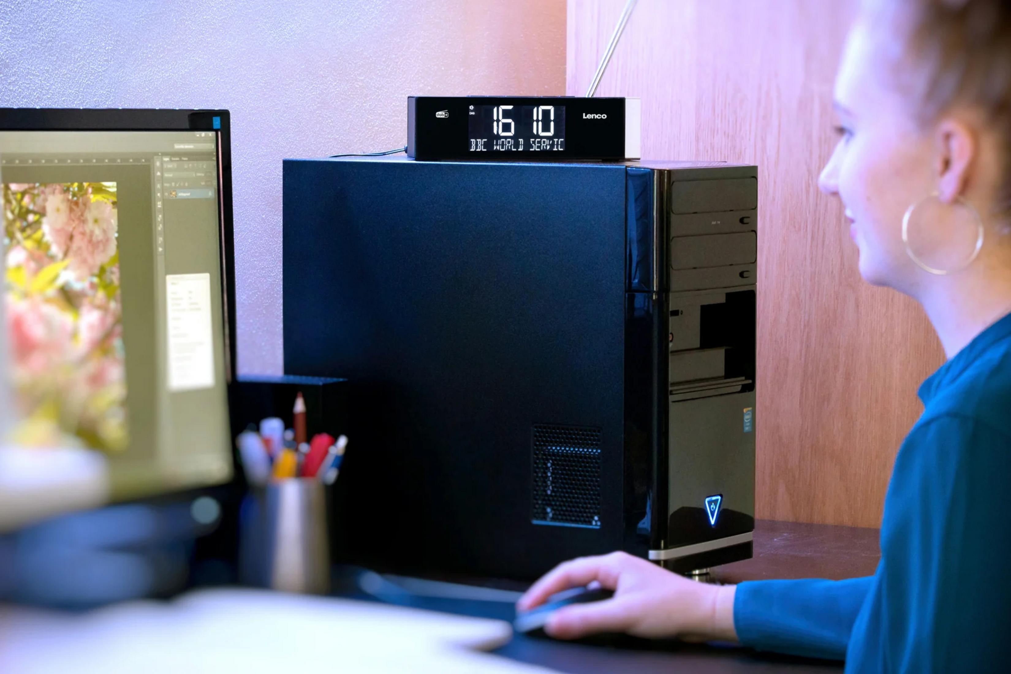Een vrouw gebruikt een computer met een digitale radio-wekker bovenop de pc-kast.