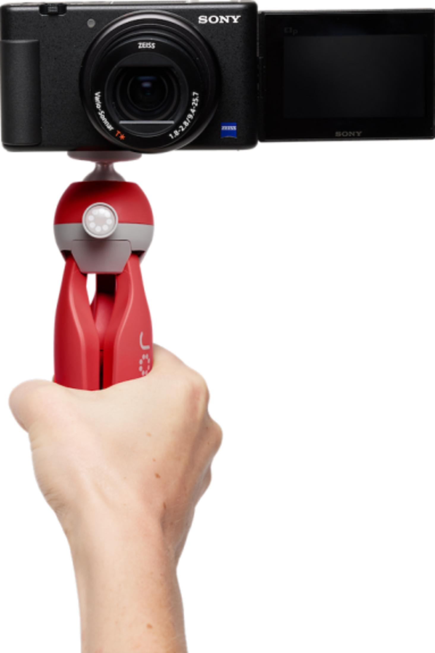 A hand holds a red camera mount with a Sony camera attached.