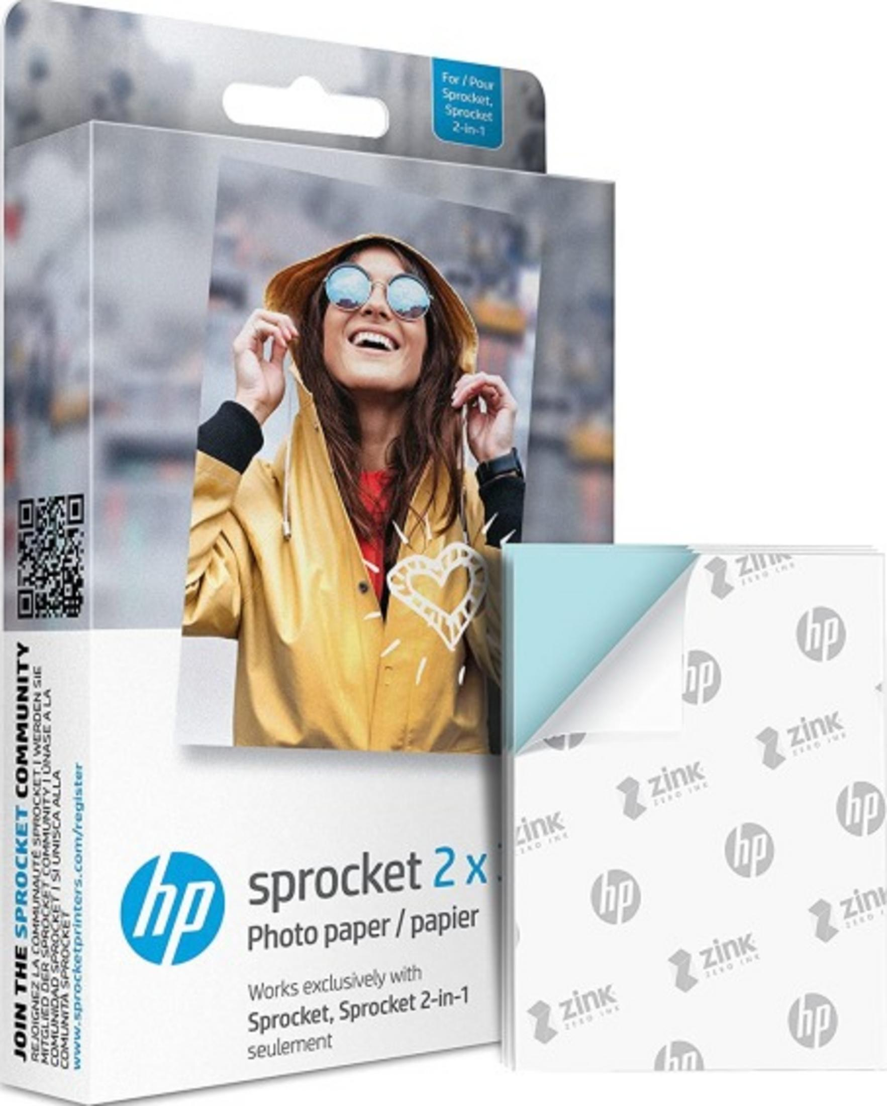 Opakowanie papieru fotograficznego HP Sprocket z kobietą w żółtej kurtce przeciwdeszczowej. Stos papieru Zink po prawej.