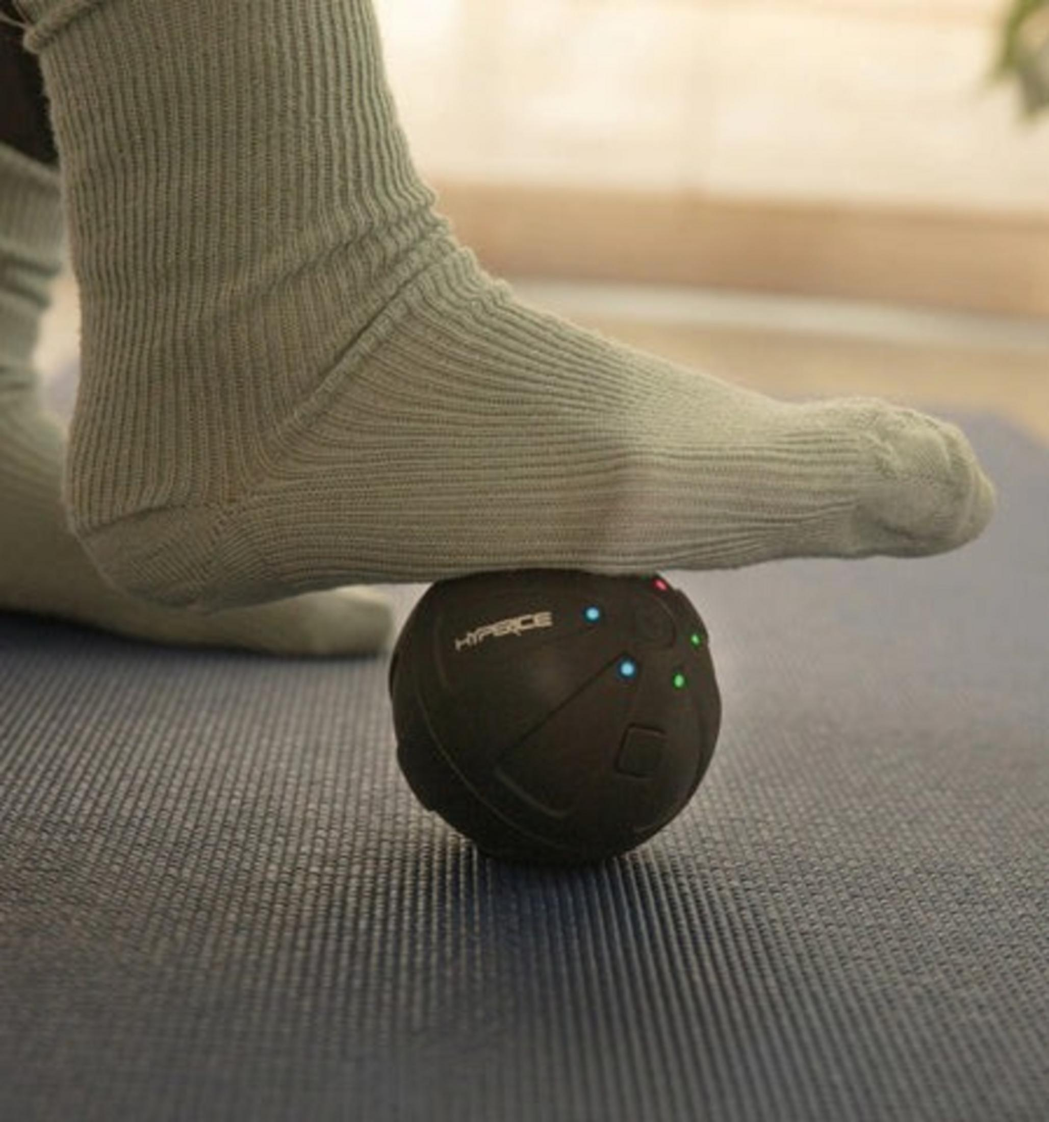 Ein Fuß in einem grauen Socken rollt über einen schwarzen Ball auf einer Matte.