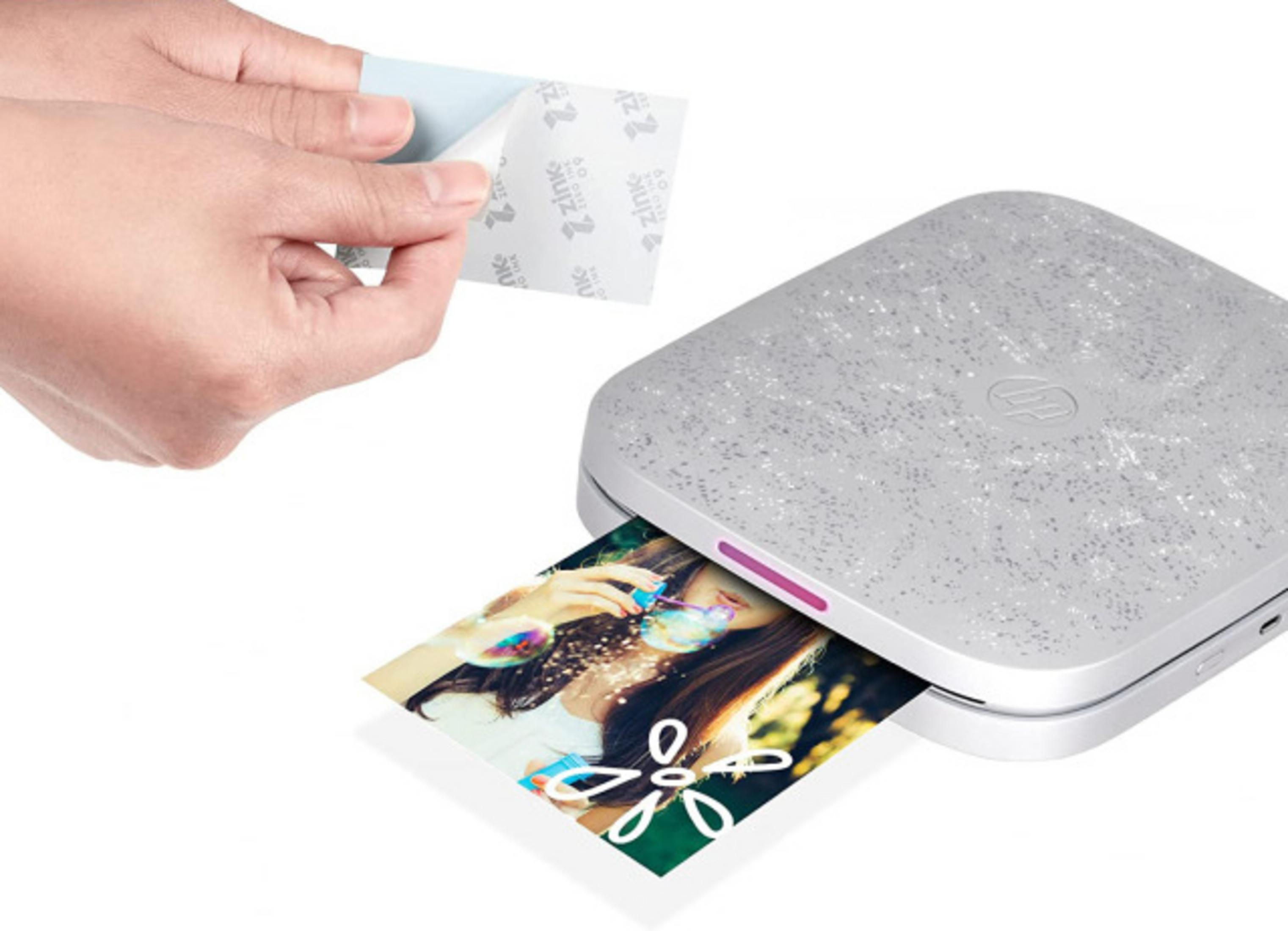 Dłoń zdejmuje papier Zink z małej, srebrnej drukarki. Drukuje się zdjęcie.