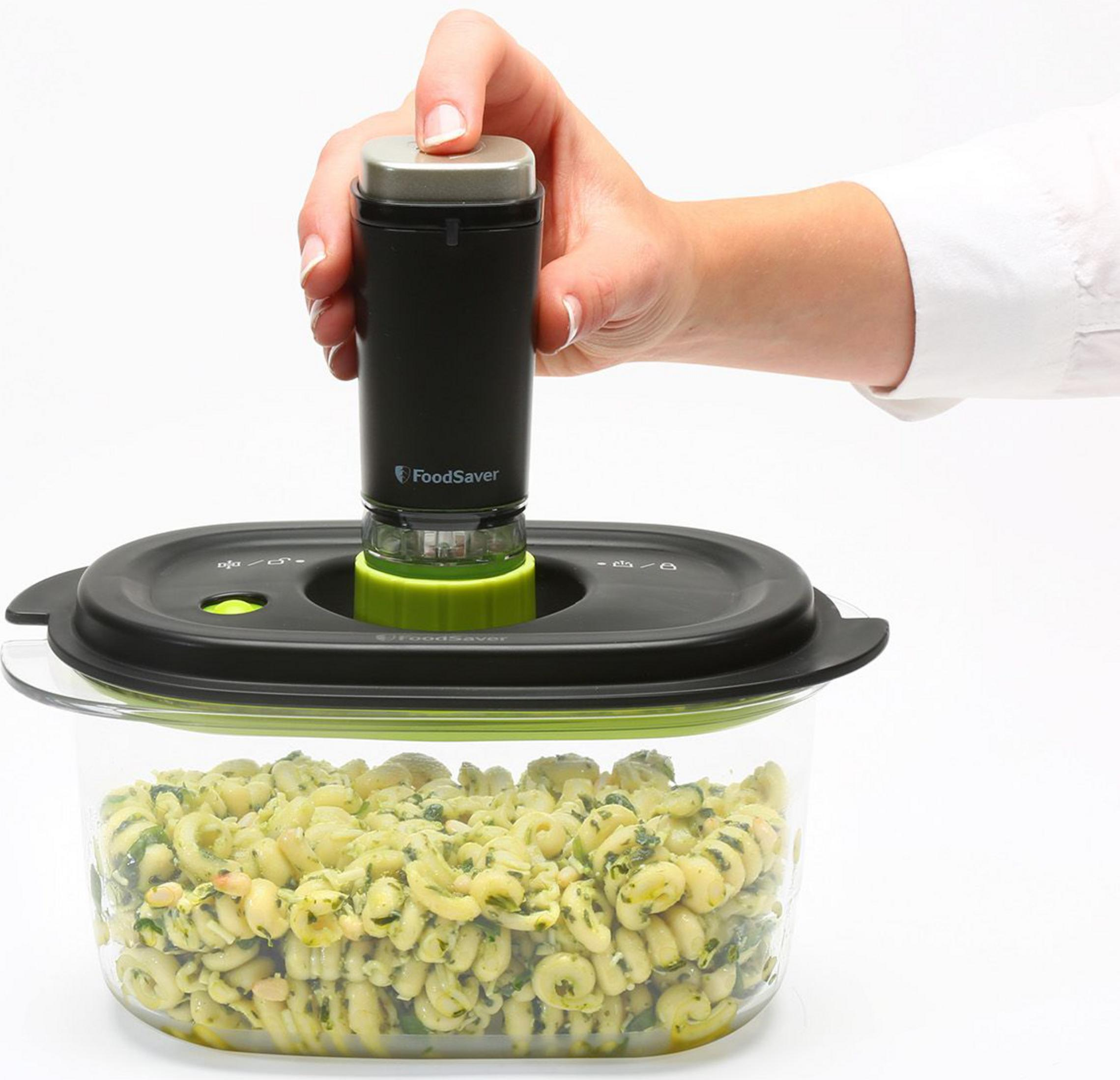 Una mano opera un sellador al vacío negro sobre un recipiente de ensalada de pasta.