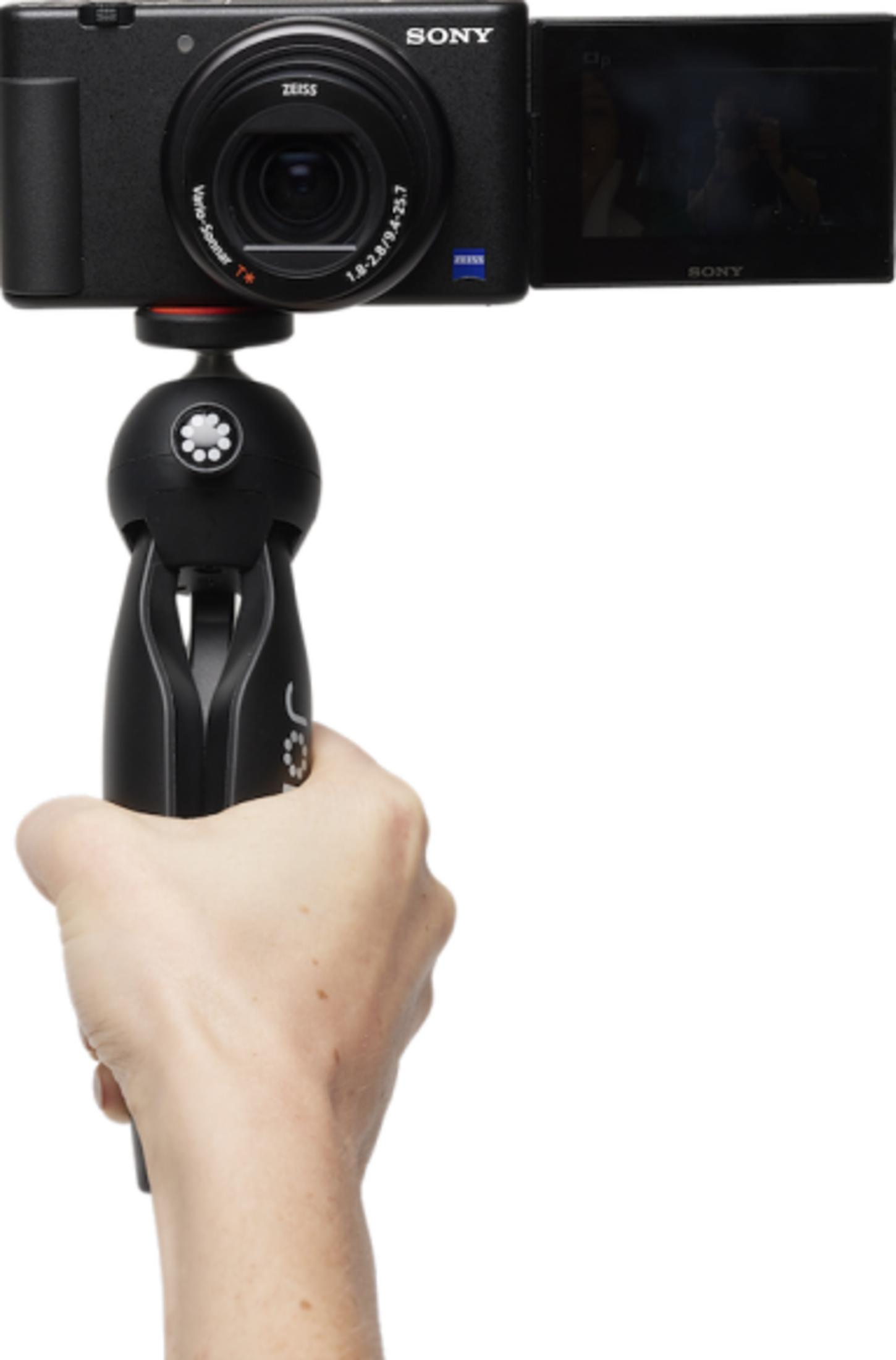 A hand holds a black Sony camera with a flip-out screen.