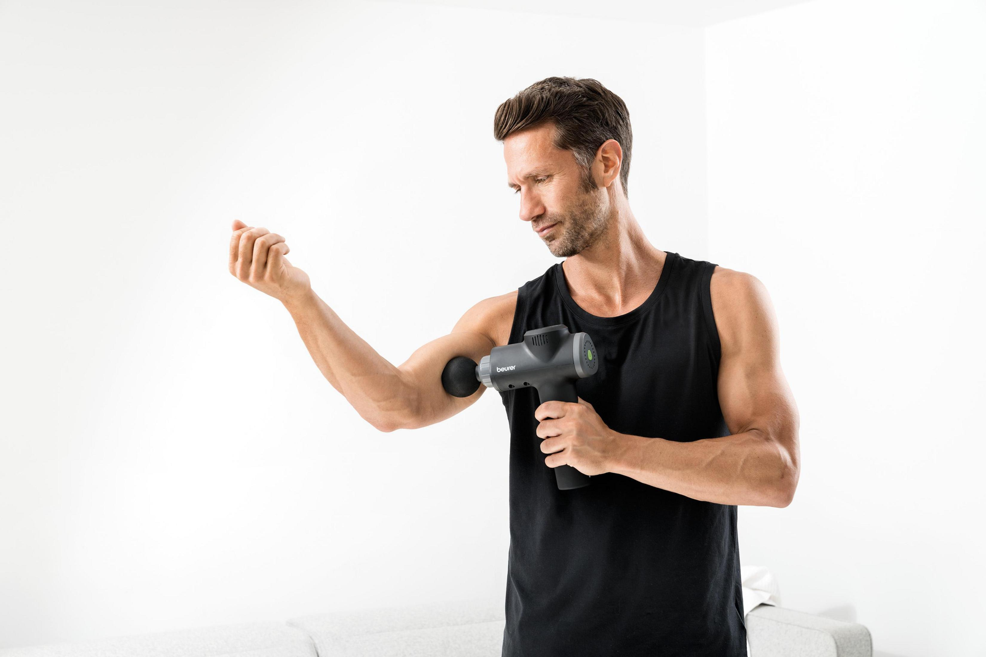 Ein Mann in einem schwarzen Tanktop benutzt eine Massagepistole an seinem Bizeps.