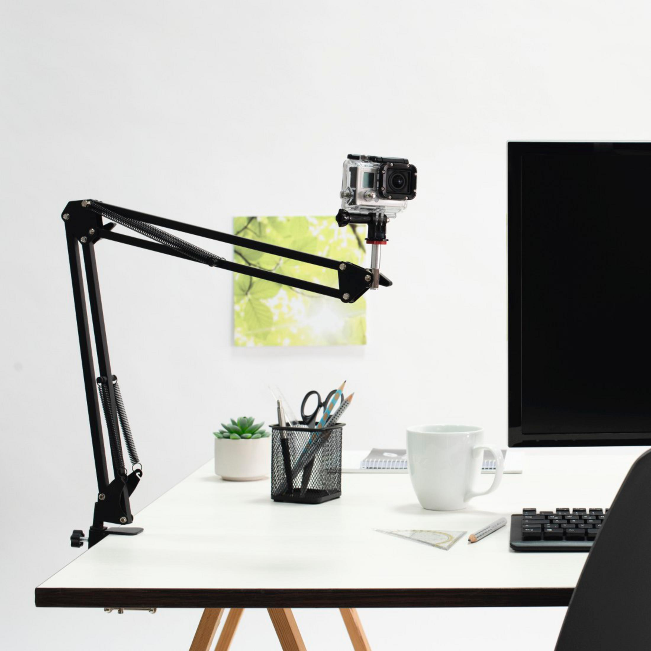 Ein Schreibtisch mit einem Scherenarm, einer Kamera, einem Monitor, einer Tasse und Büromaterial.