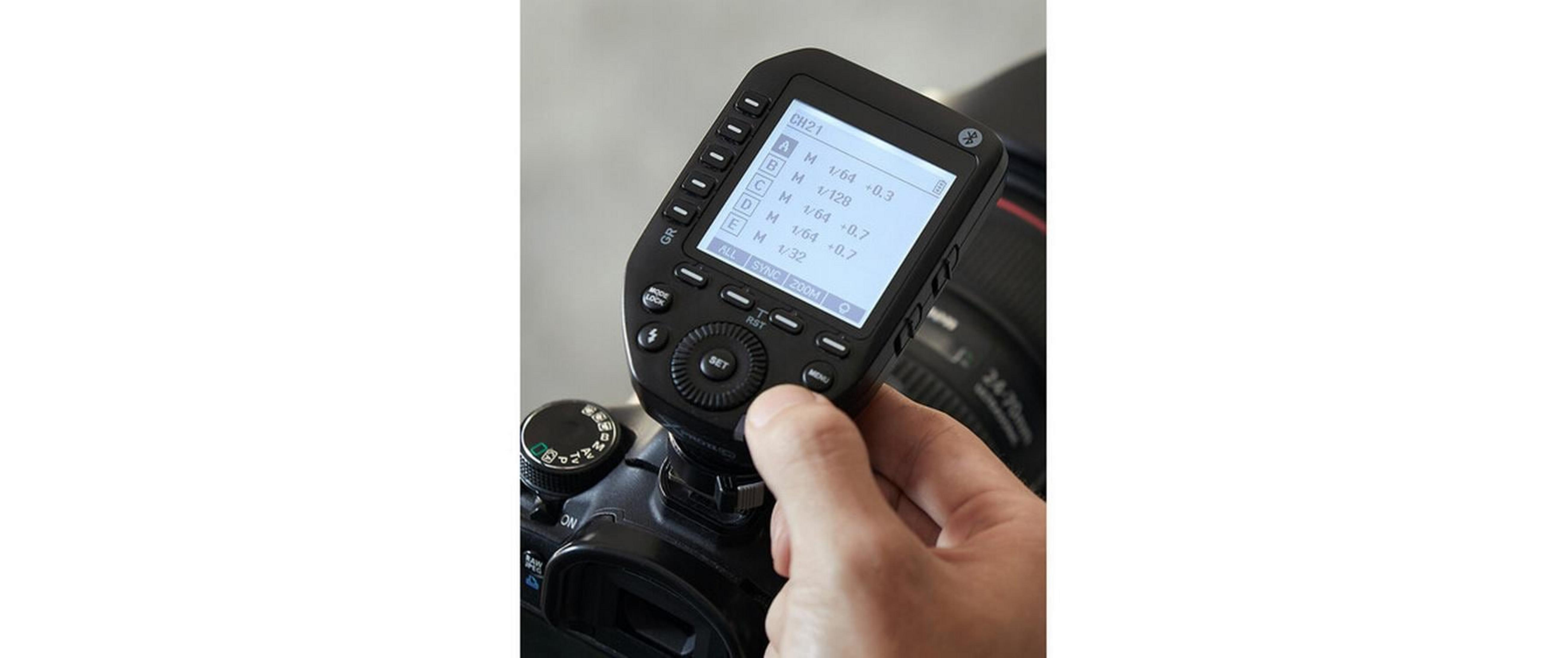 Une main actionne un appareil photo avec un flash externe affichant un écran LCD.