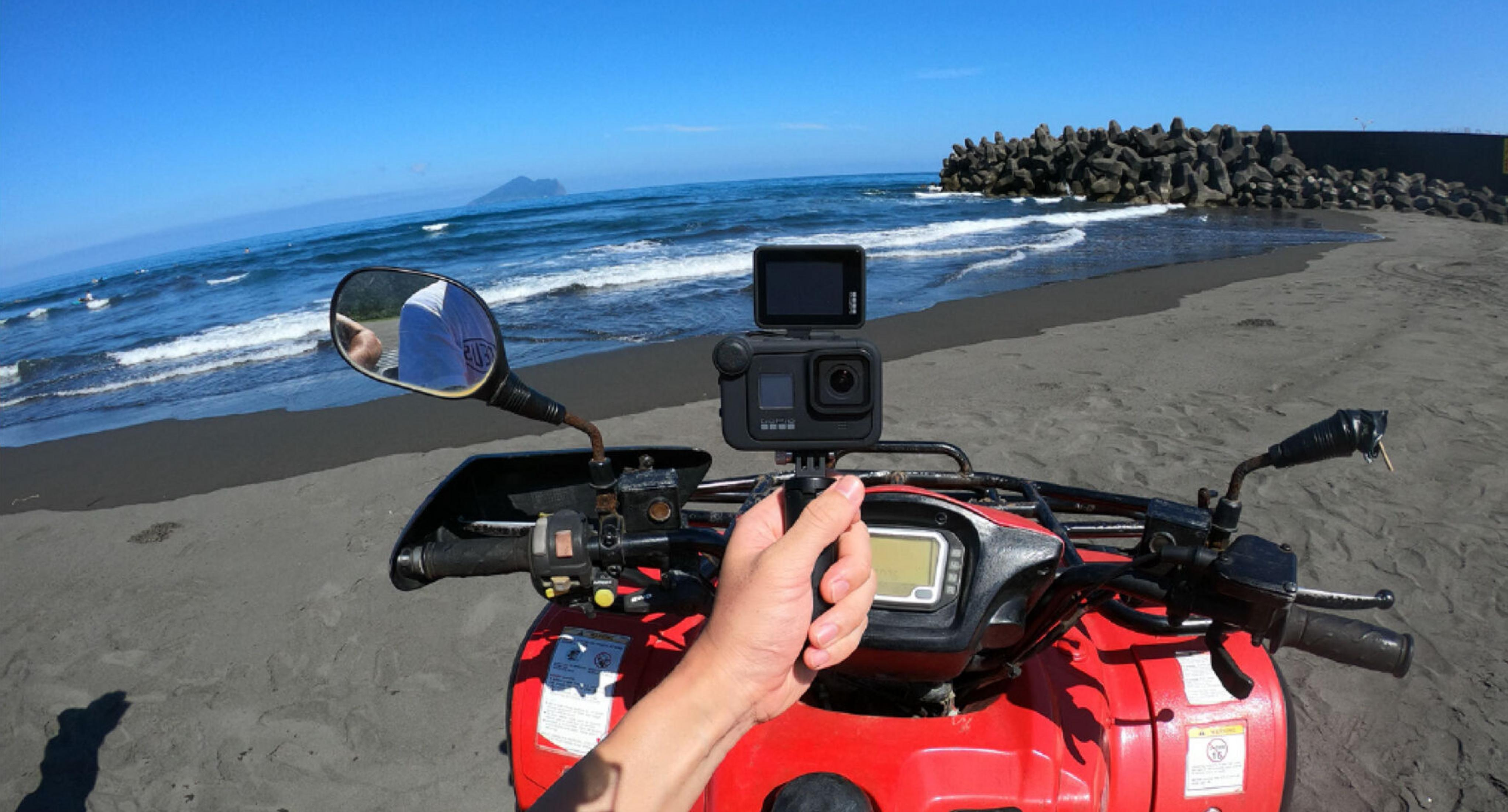 Un quad rosso con GoPro sulla spiaggia, di fronte al mare e alle onde.