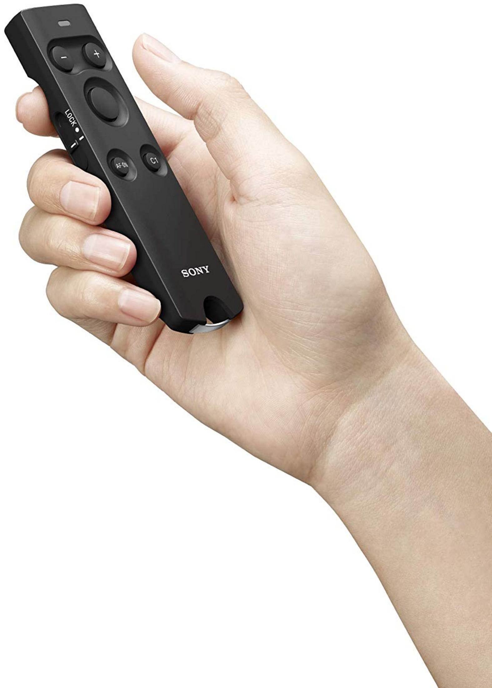 Dłoń trzyma czarny pilot Sony z przyciskami i przełącznikiem.