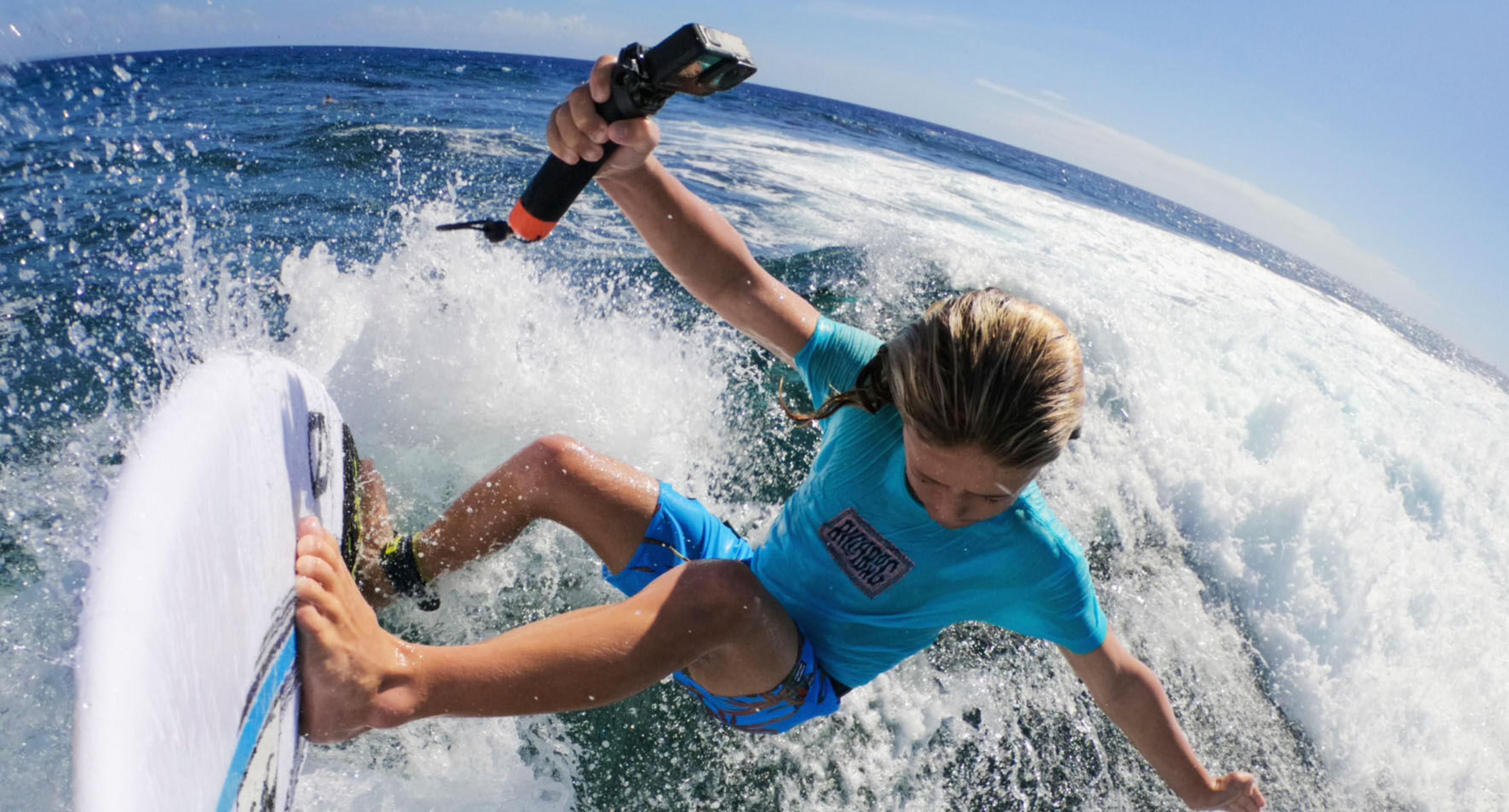 Chłopiec surfuje na desce, trzymając kamerę w dłoni.