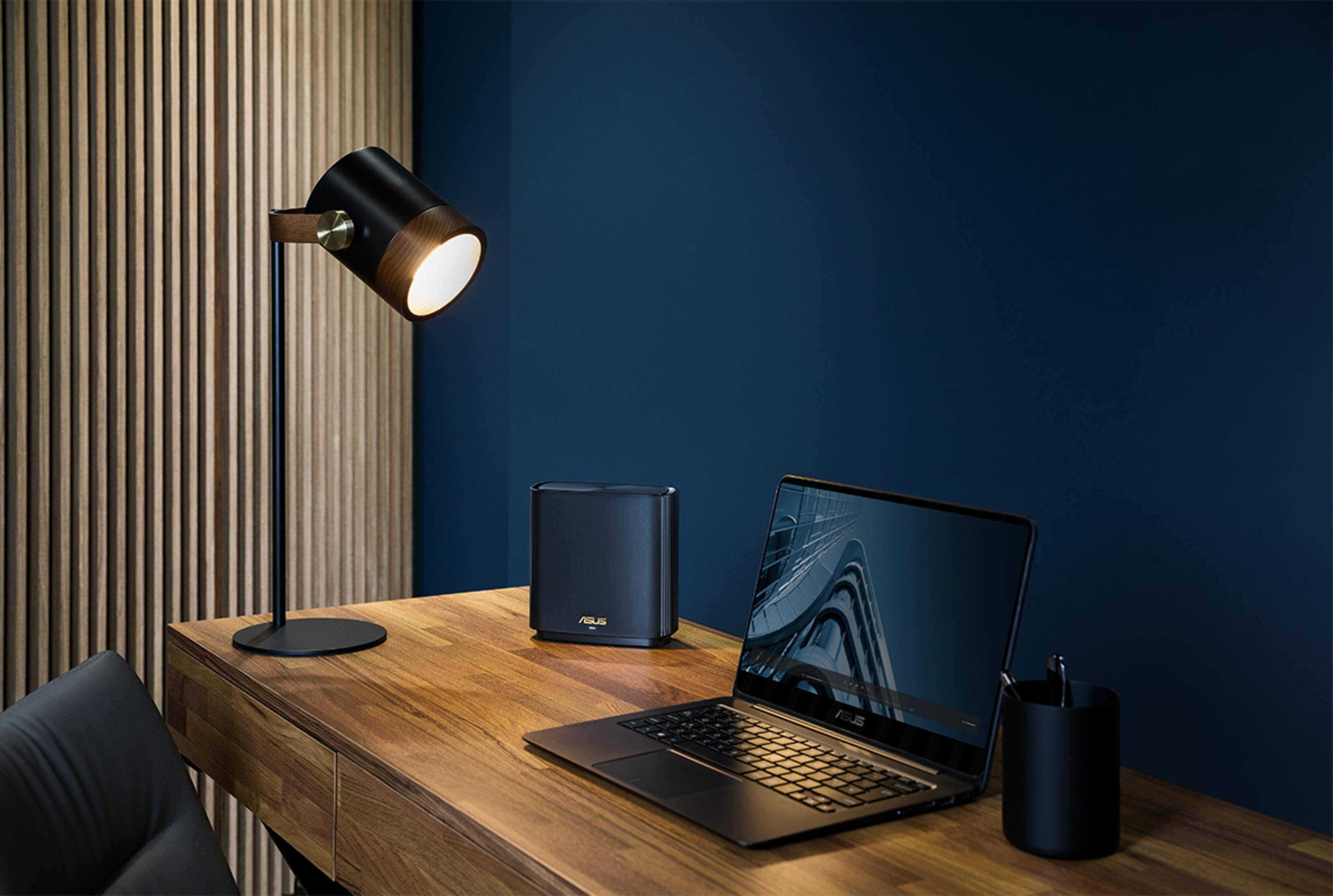 Biurko z laptopem, routerem i lampą na tle niebieskiej ściany.