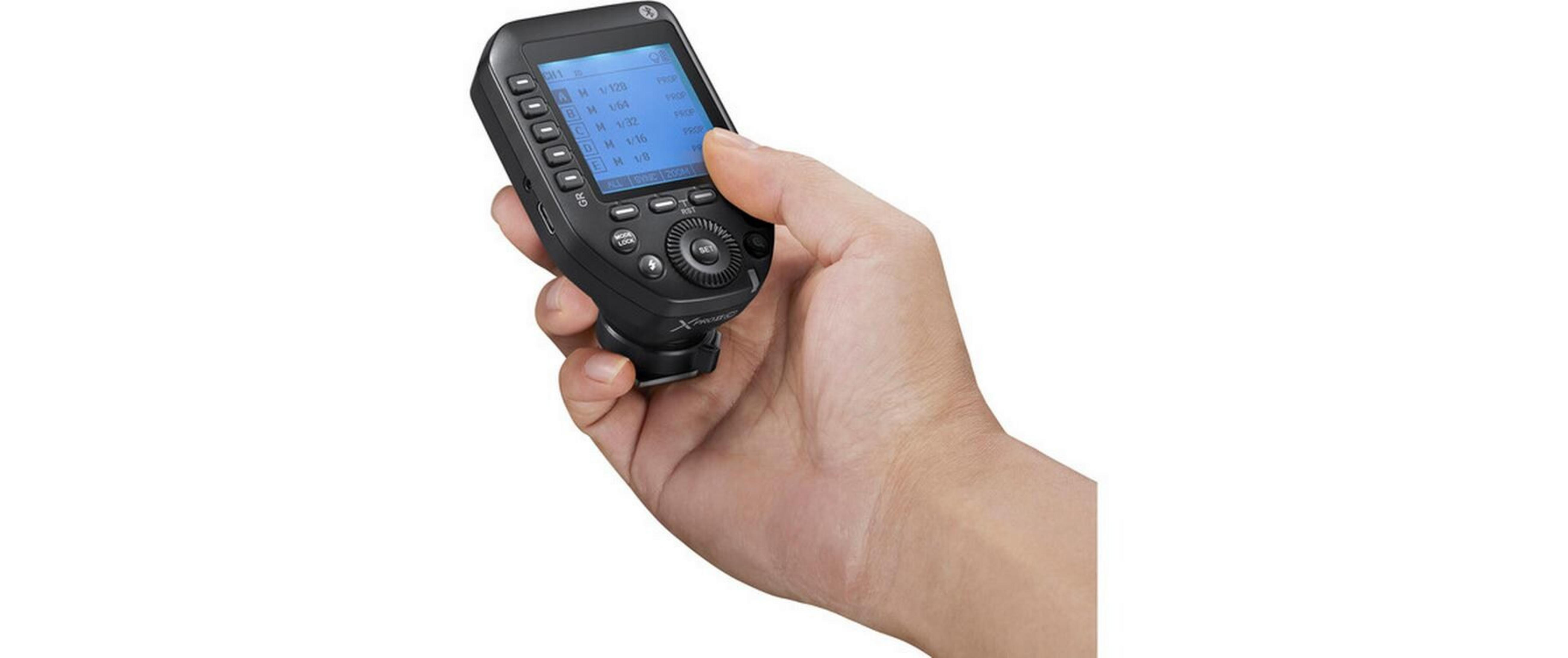 Una mano sostiene un controlador de flash de cámara negro con pantalla azul.