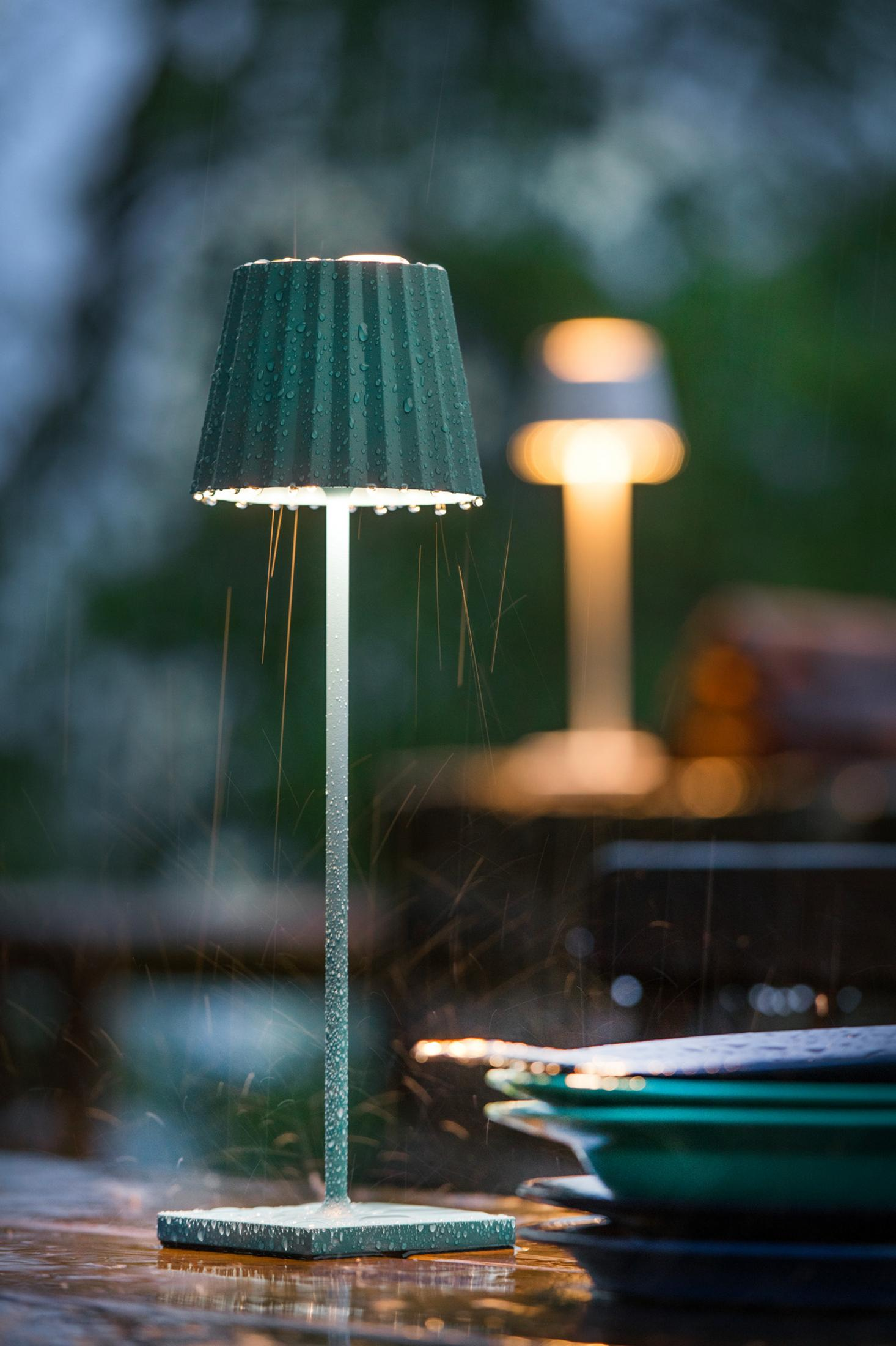 Una lampada verde con gocce d'acqua sotto la pioggia, un'altra lampada sullo sfondo.