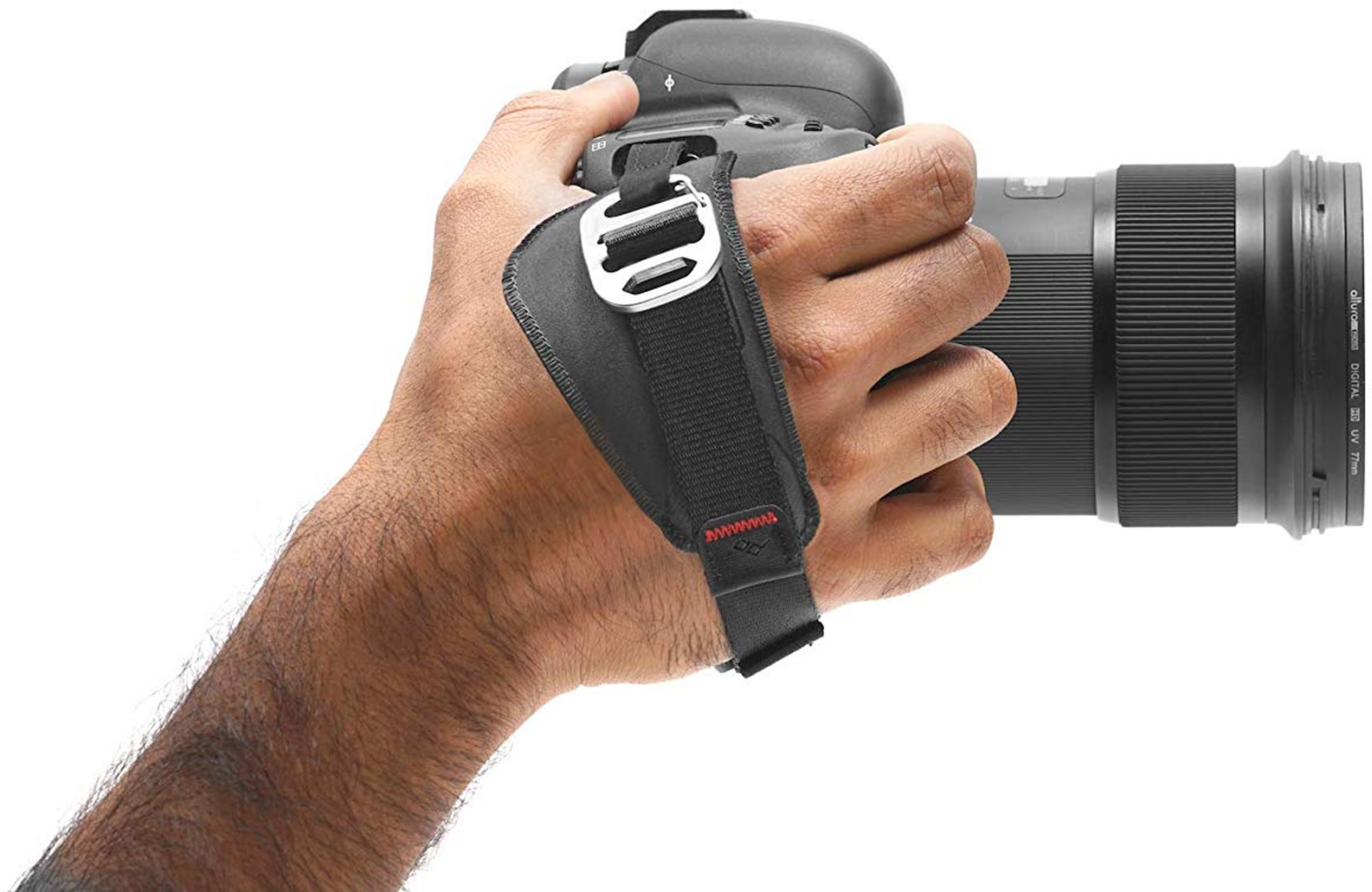 Dłoń trzyma aparat z obiektywem i czarnym paskiem.