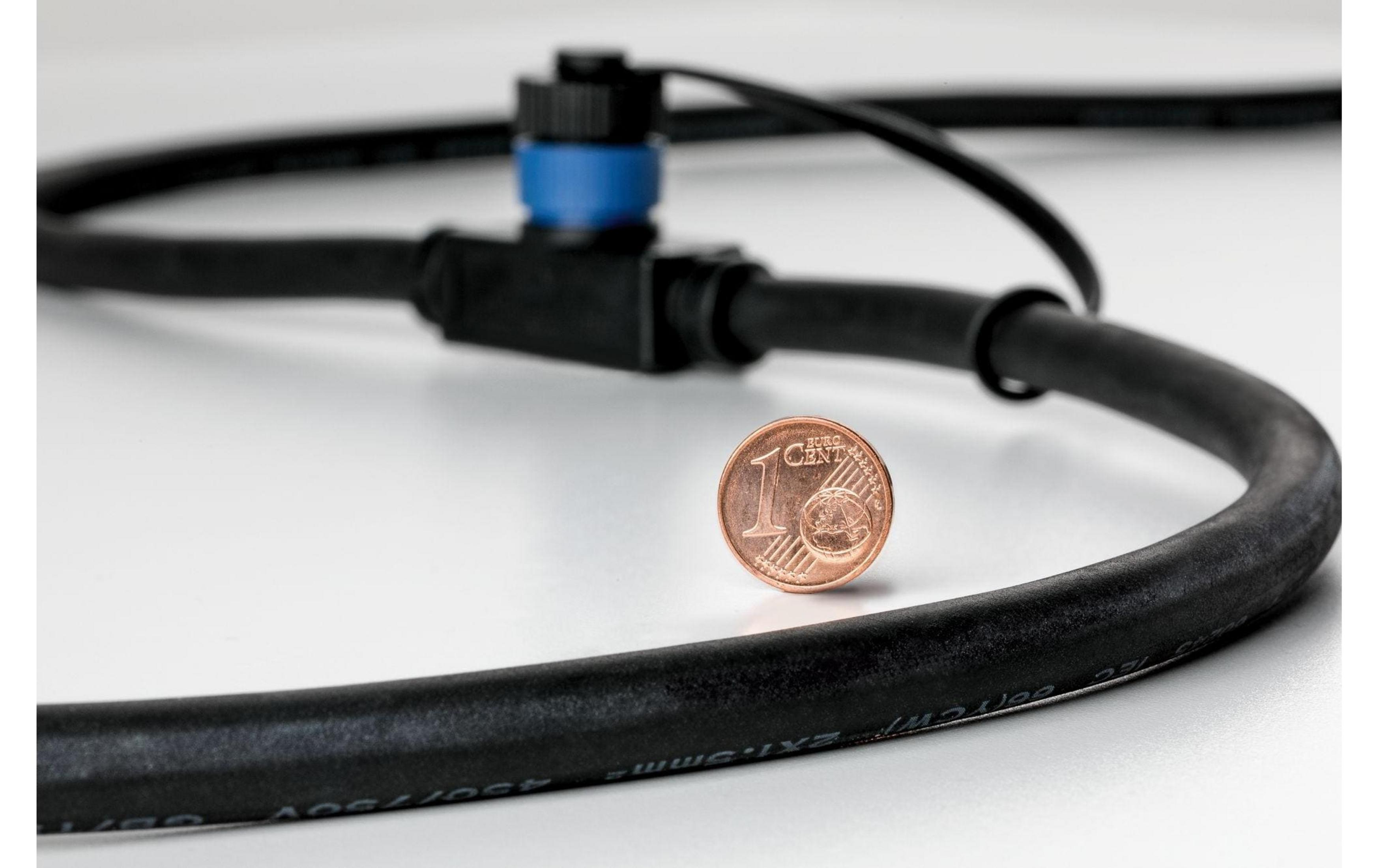 Eine Ein-Cent-Münze liegt neben einem schwarzen Kabel mit blauem Stecker.