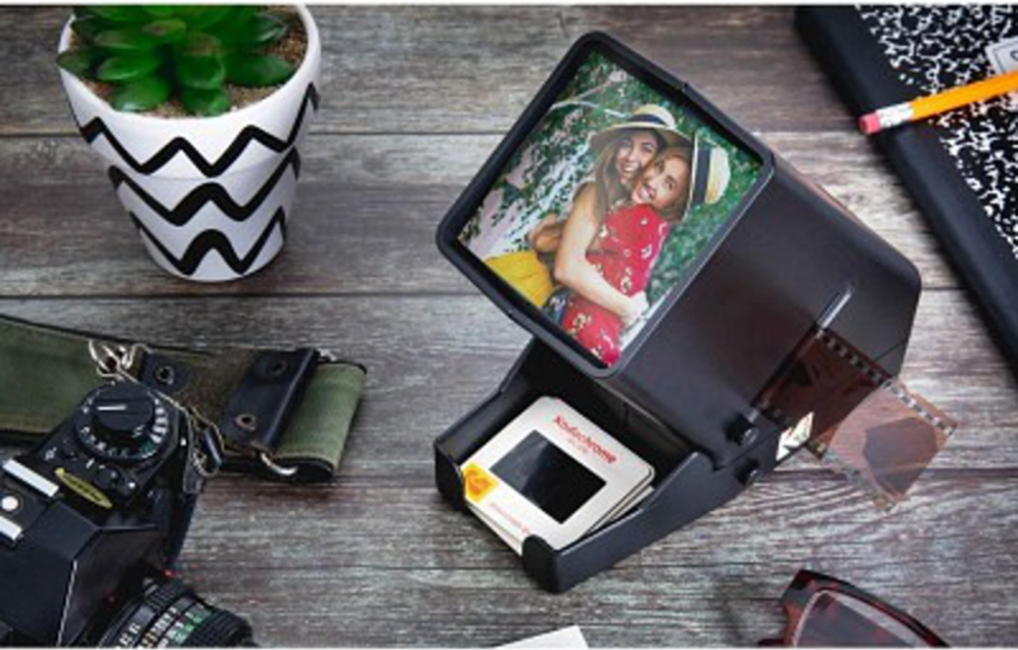 Una fotocamera, un vaso per piante e un proiettore di diapositive con foto su tavolo di legno.
