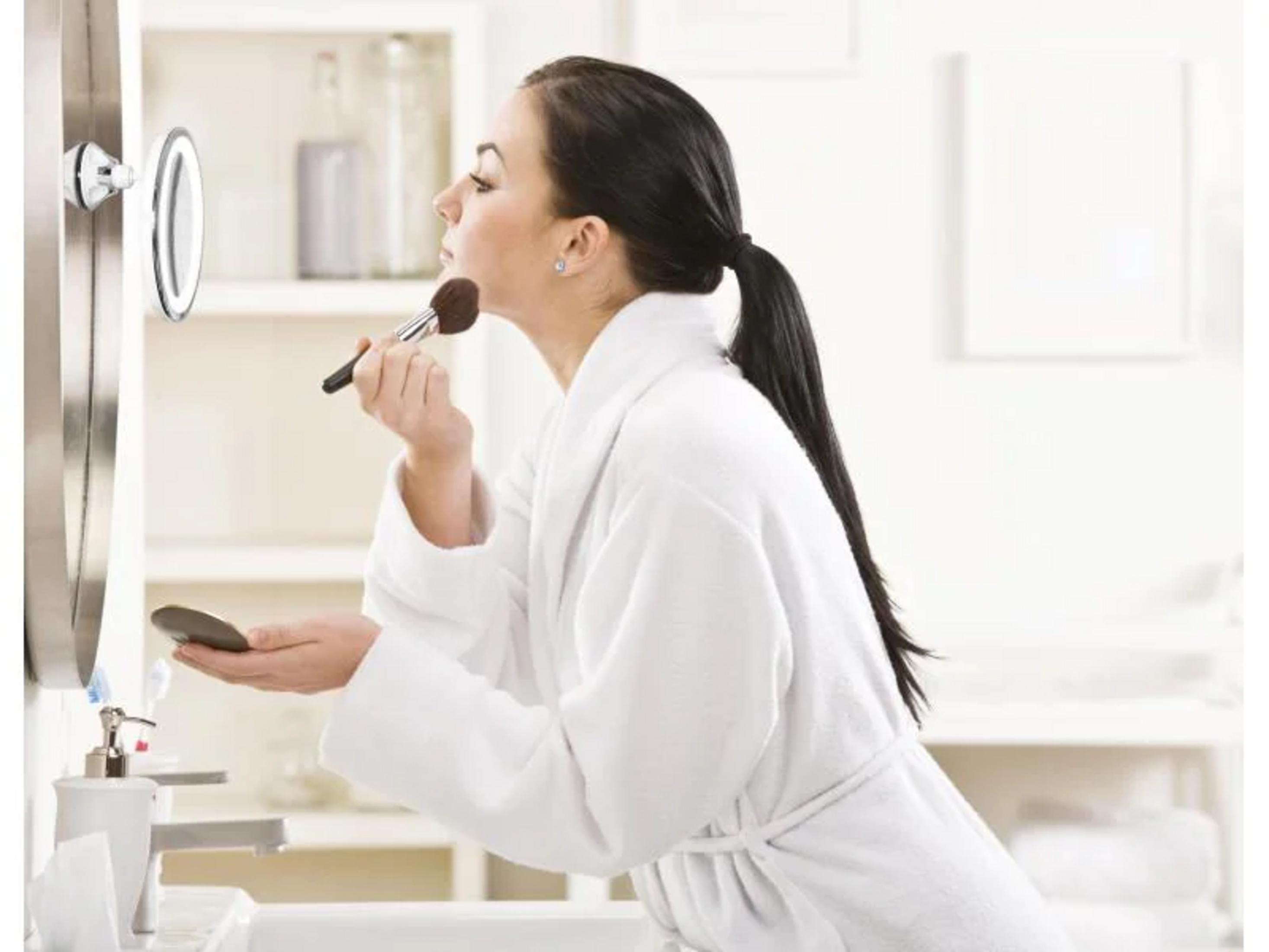 Eine Frau in einem weißen Bademantel trägt Make-up auf.