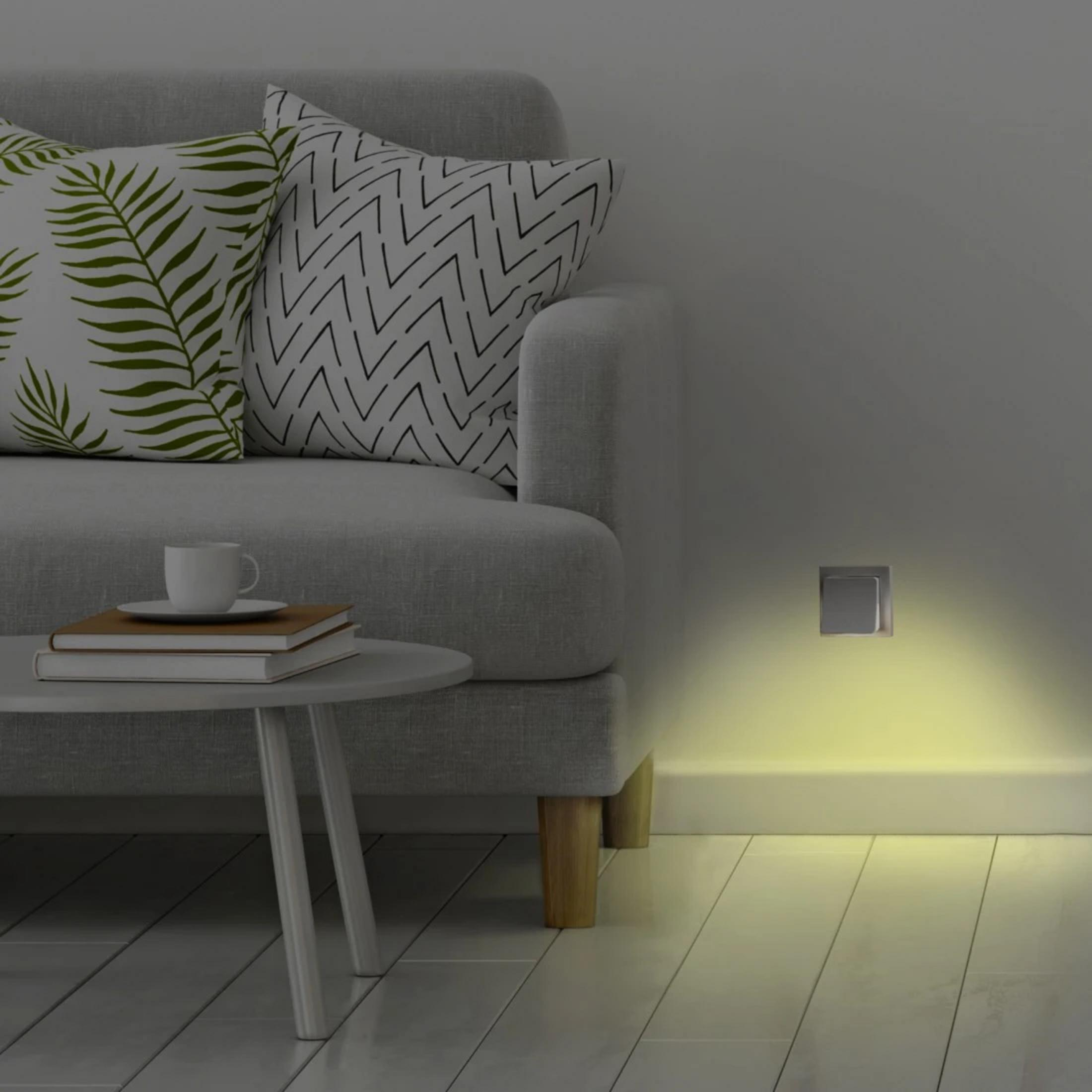 Szara sofa z poduszkami, stolik boczny z książkami i filiżanką kawy, kinkiet.