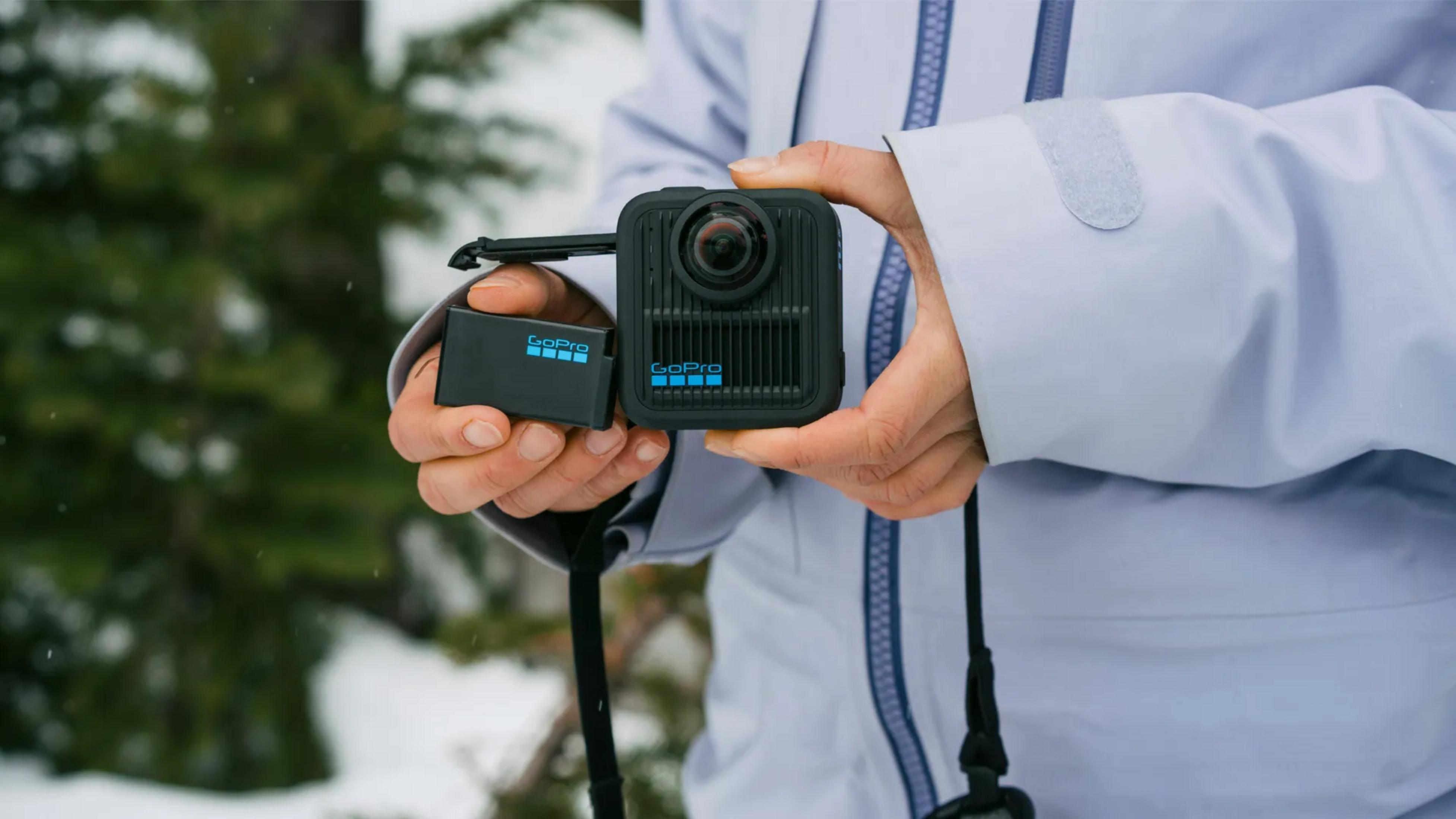 Person hält GoPro-Kamera und Akku in verschneiter Landschaft.