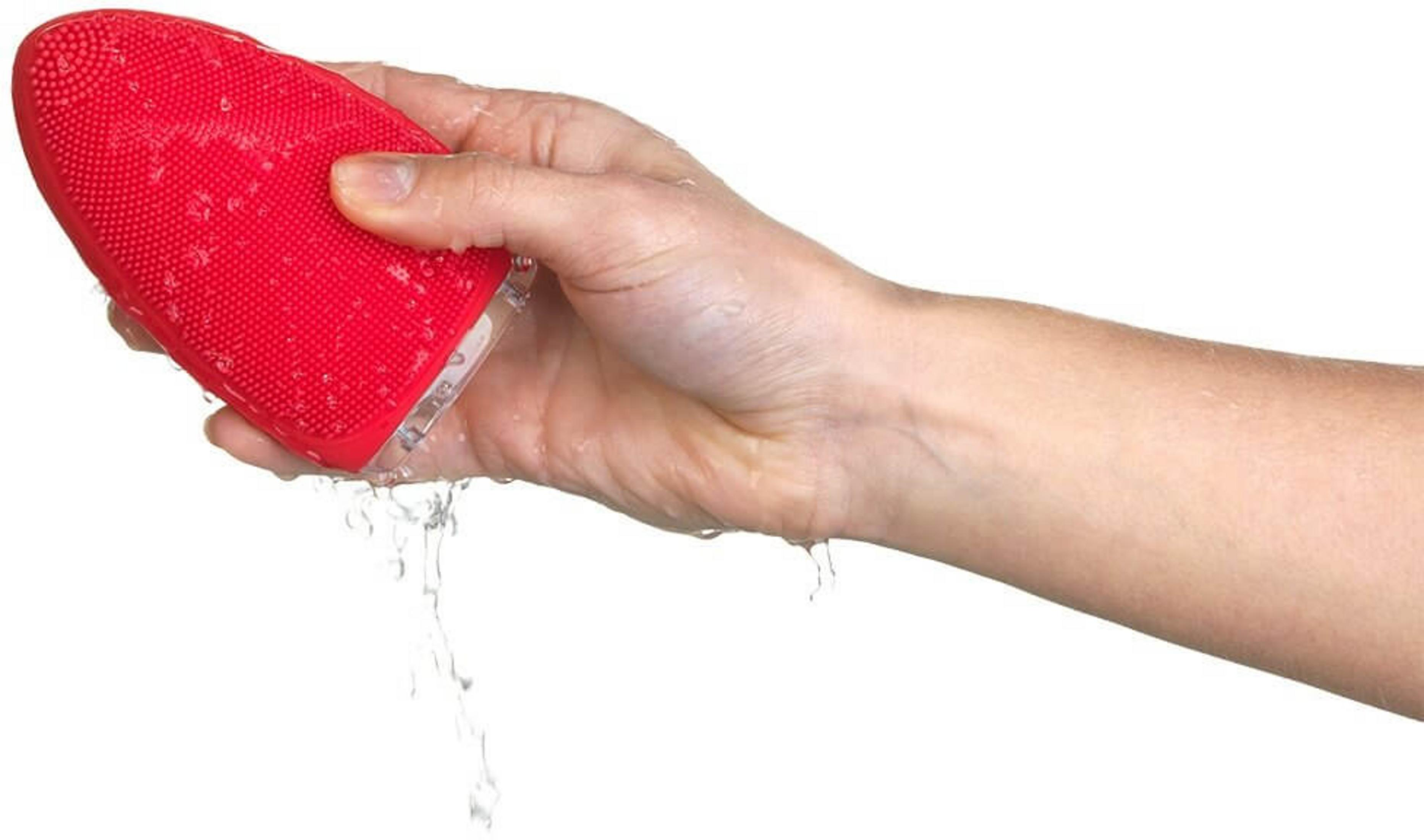 Eine Hand hält eine rote Silikonbürste, aus der Wasser tropft.