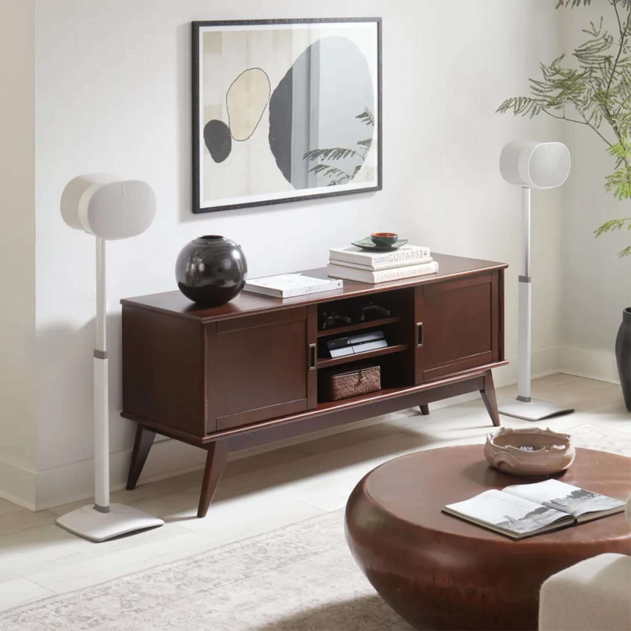 Ein Wohnzimmer mit dunklem Holzschrank, zwei weißen Lautsprechern und einem runden Tisch.