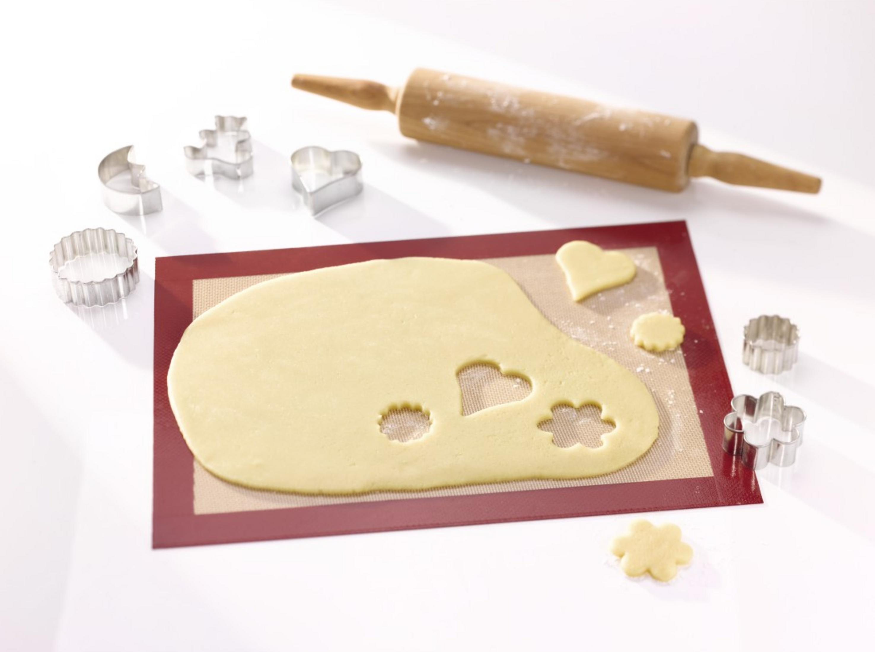 Holz-Nudelholz und Ausstecher auf Teig auf Silikonmatte. Herz, Blume, Mond, Bär.