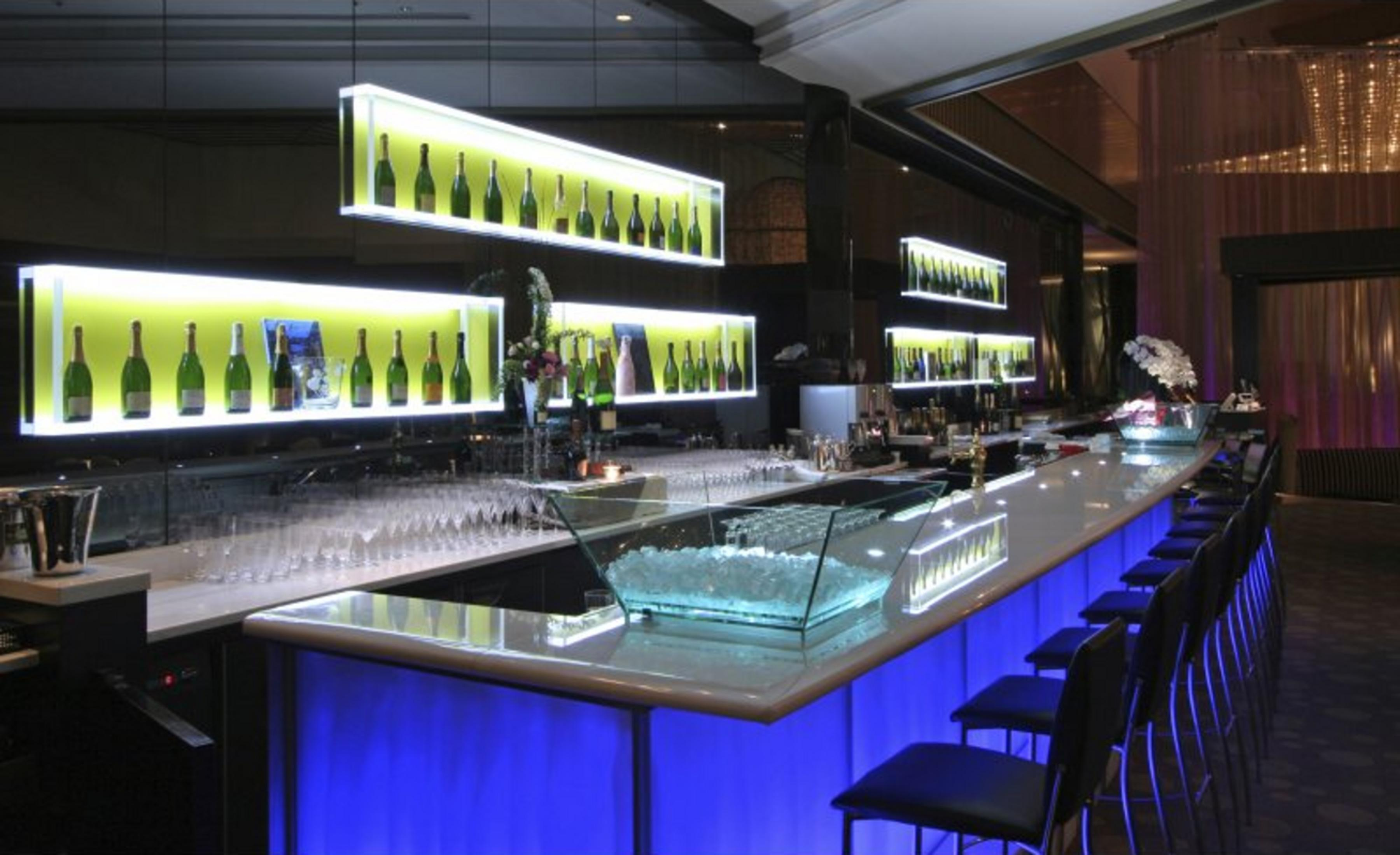 Eine beleuchtete Bar mit Flaschen in Regalen, Gläsern und blauen Lichtern.