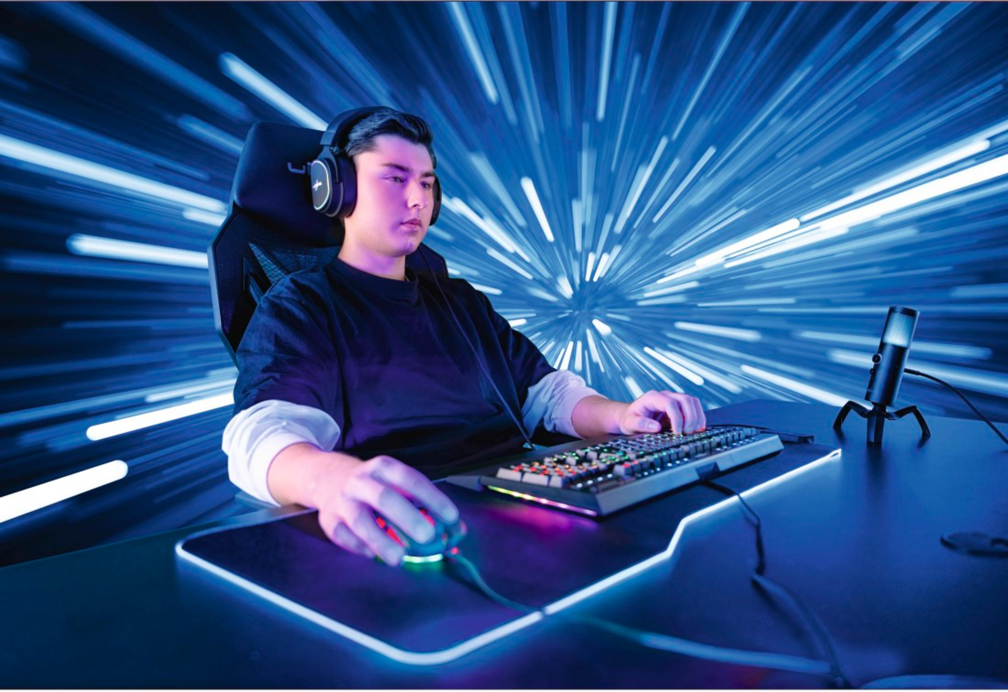 Ein junger Mann mit Kopfhörern spielt Videospiele an einem beleuchteten Schreibtisch.