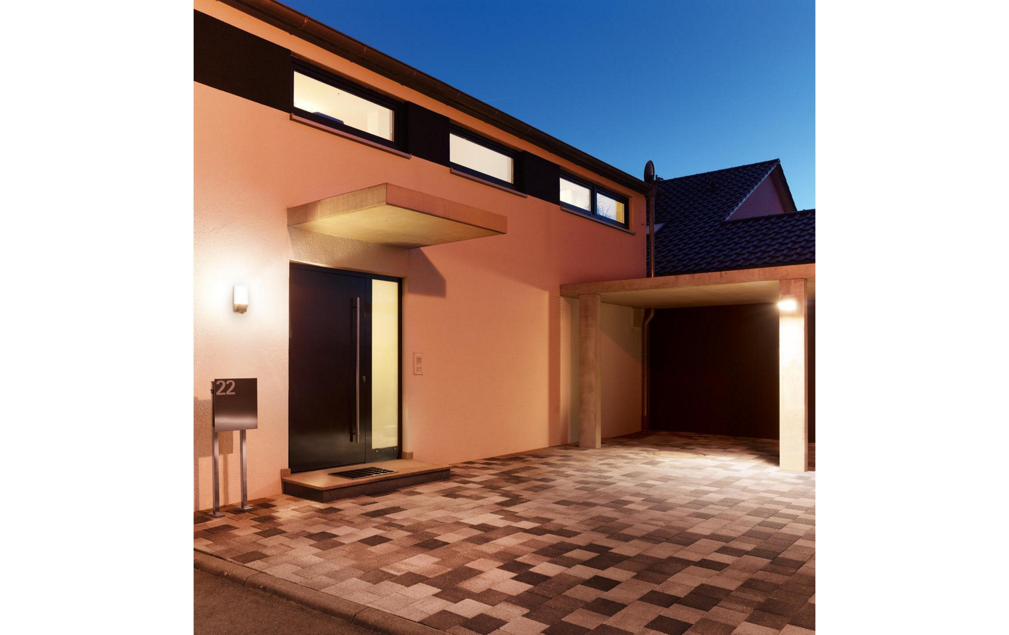 Modernes Haus mit orangefarbener Fassade, dunkler Tür und Carport bei Nacht.