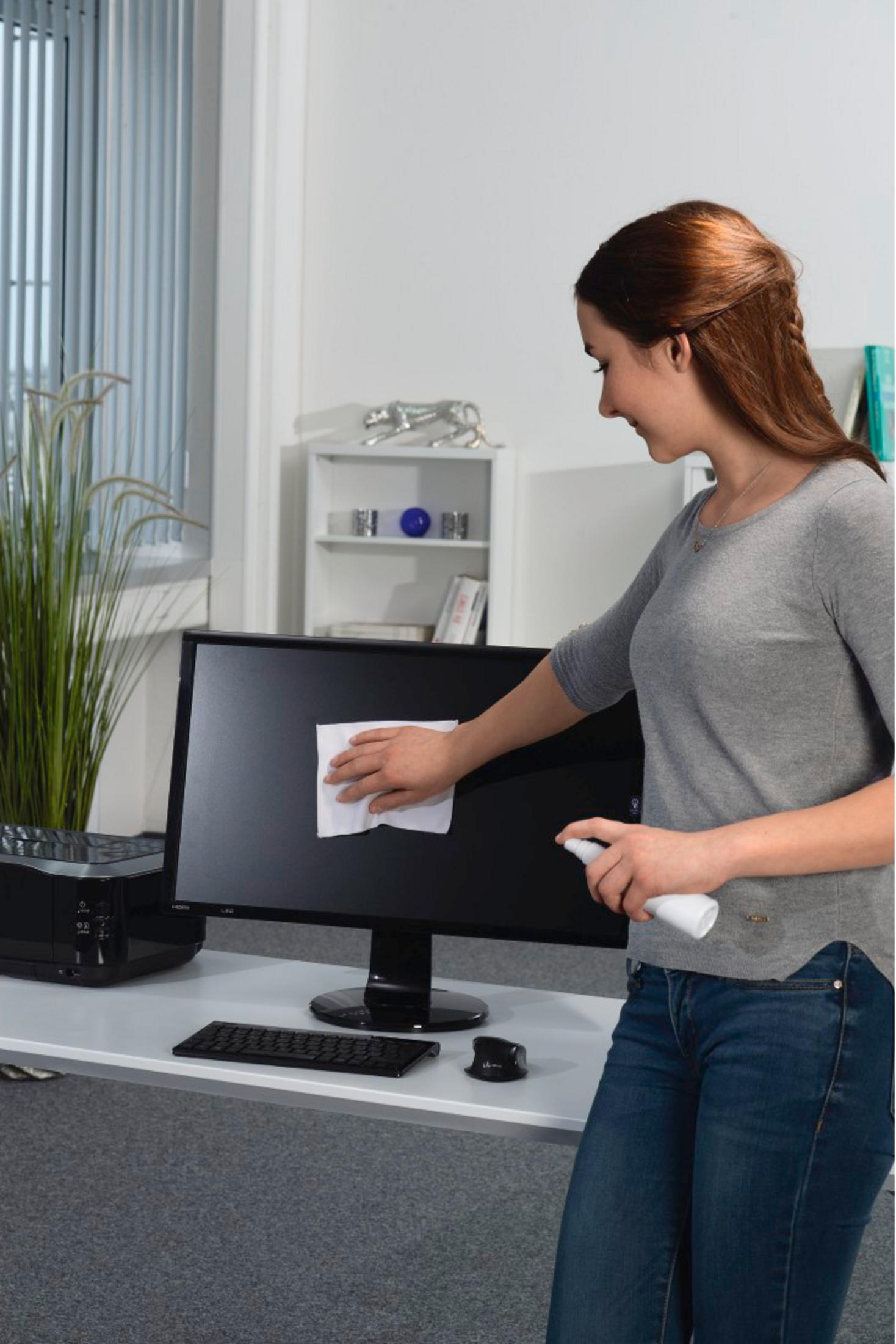 Kobieta czyści monitor komputera chusteczką i sprayem.