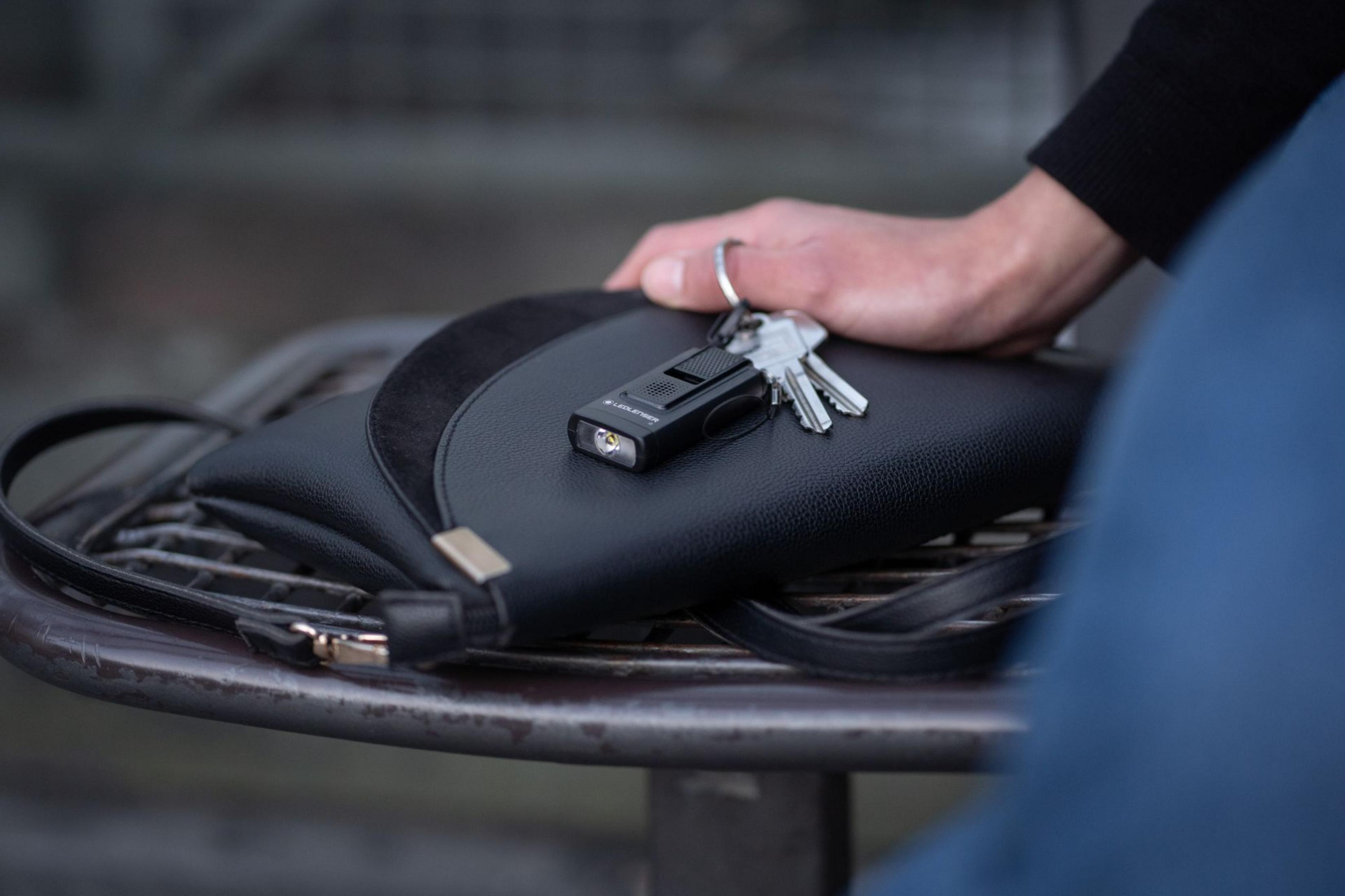 Czarna torebka z pękiem kluczy i małą latarką na metalowym stole.