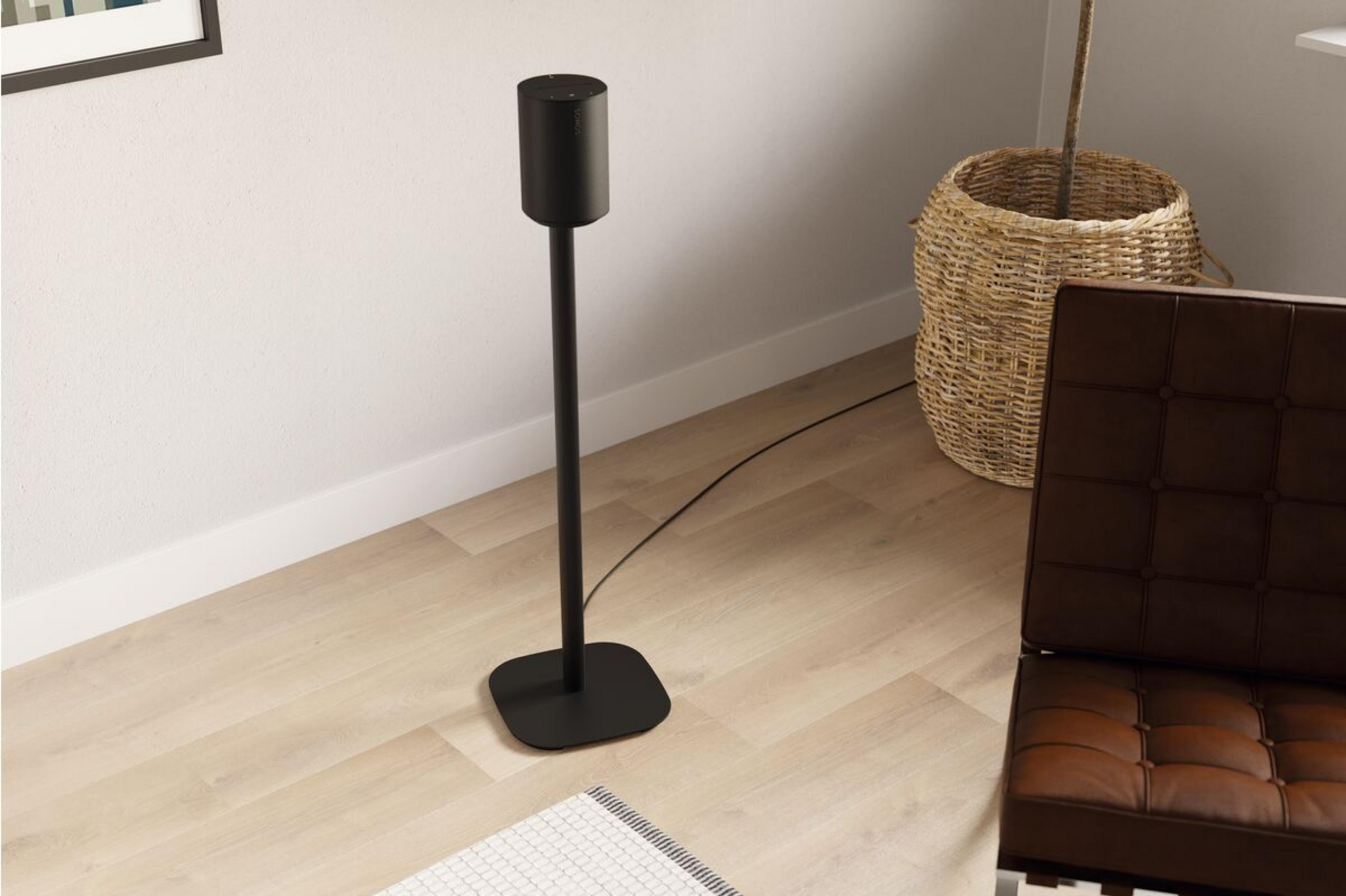 Une enceinte noire sur un pied fin près d'un panier en osier.