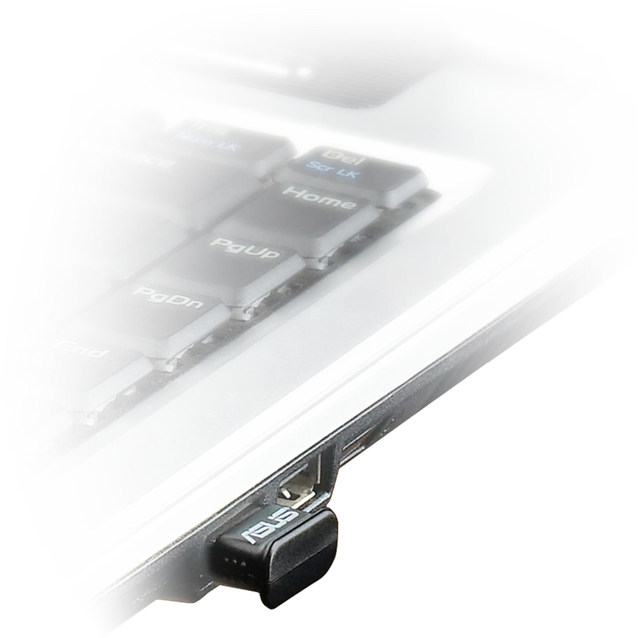 Adaptador USB ASUS negro en puerto de portátil, teclado al fondo.