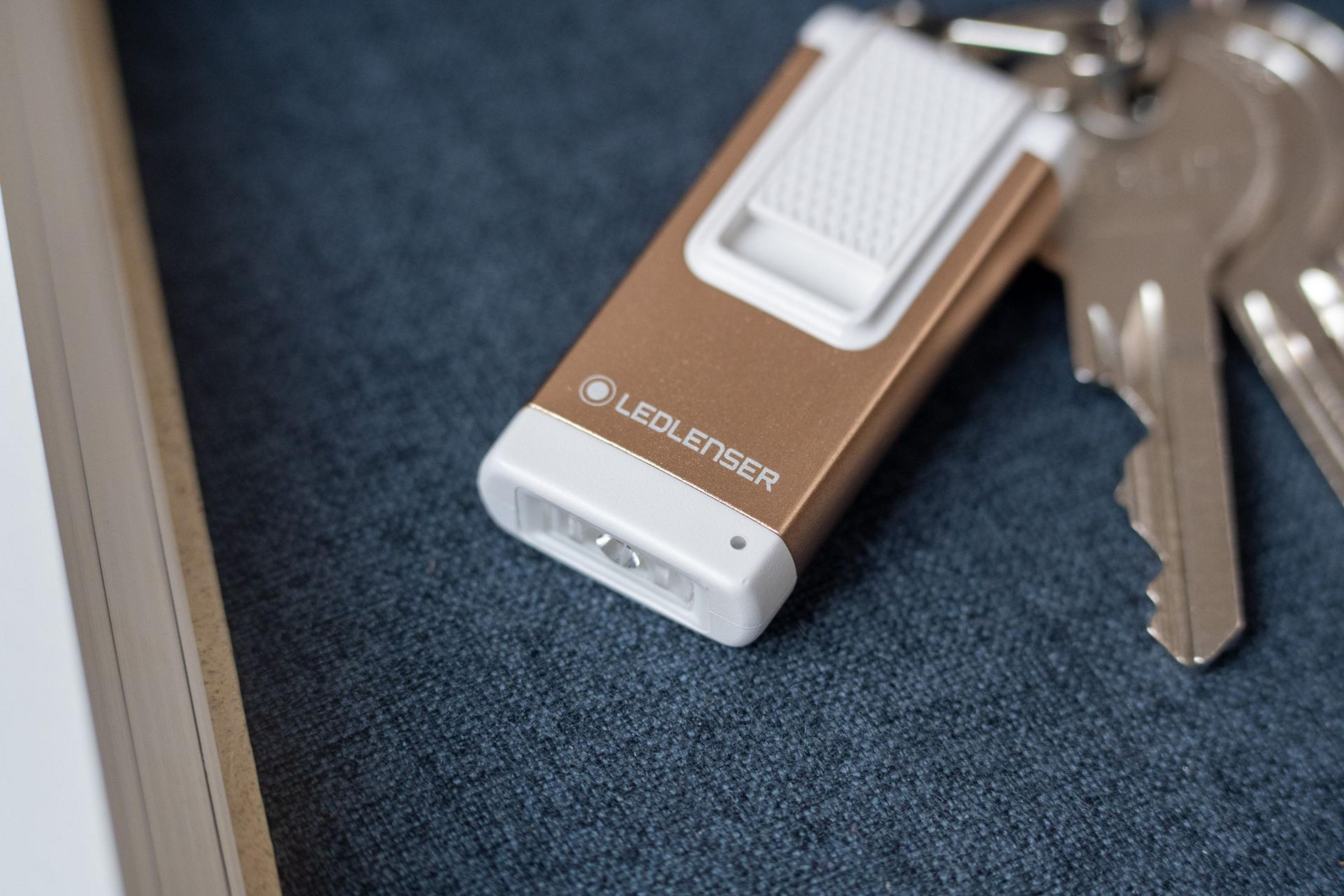 Kompaktowa, złota latarka z białym elementem i kluczami na niebieskiej tkaninie.