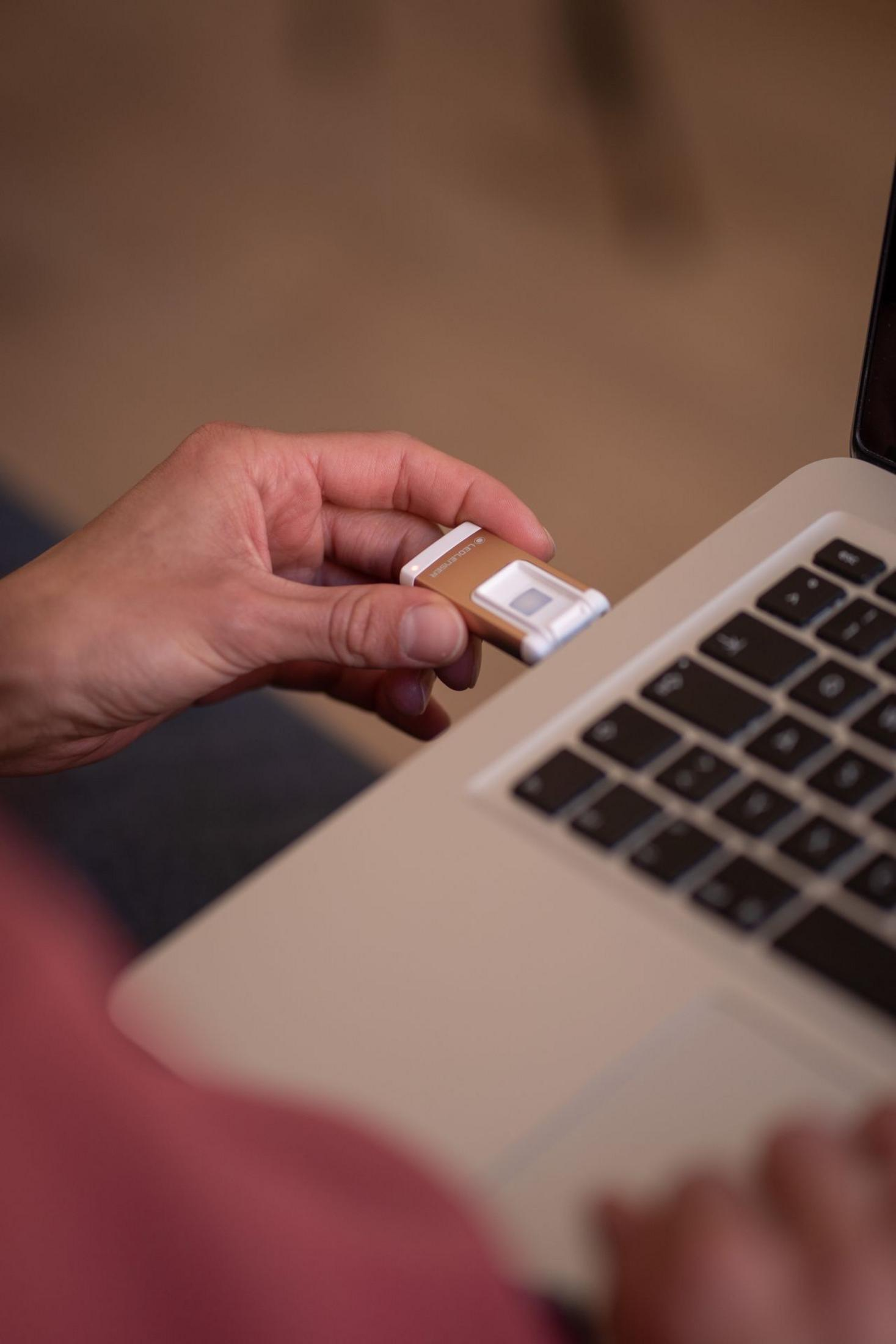Dłoń wkłada mały, brązowy pendrive do laptopa.