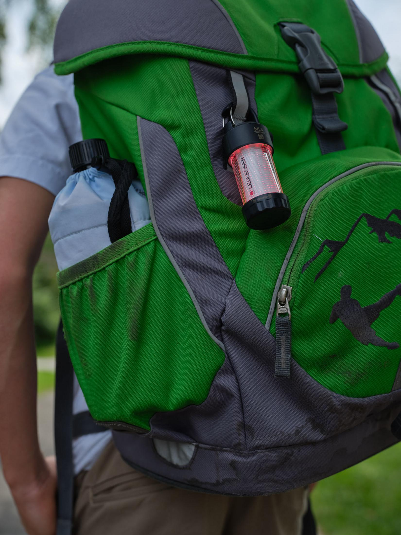 Zaino verde con una piccola lanterna rossa e una borraccia.