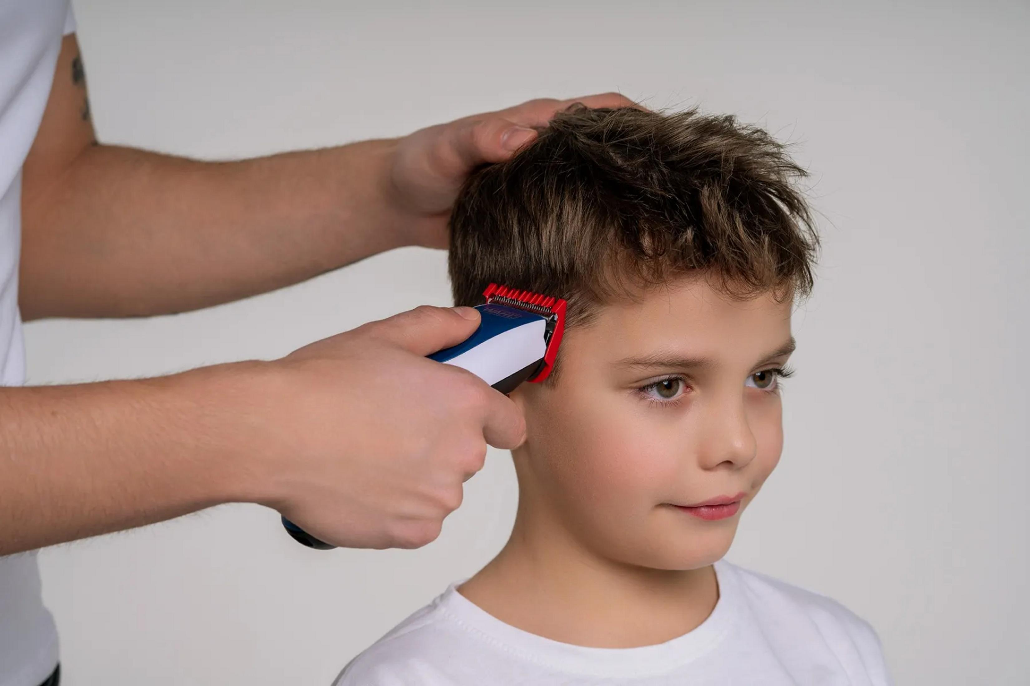 Ein Mann schneidet einem Jungen die Haare mit einem Haarschneider.