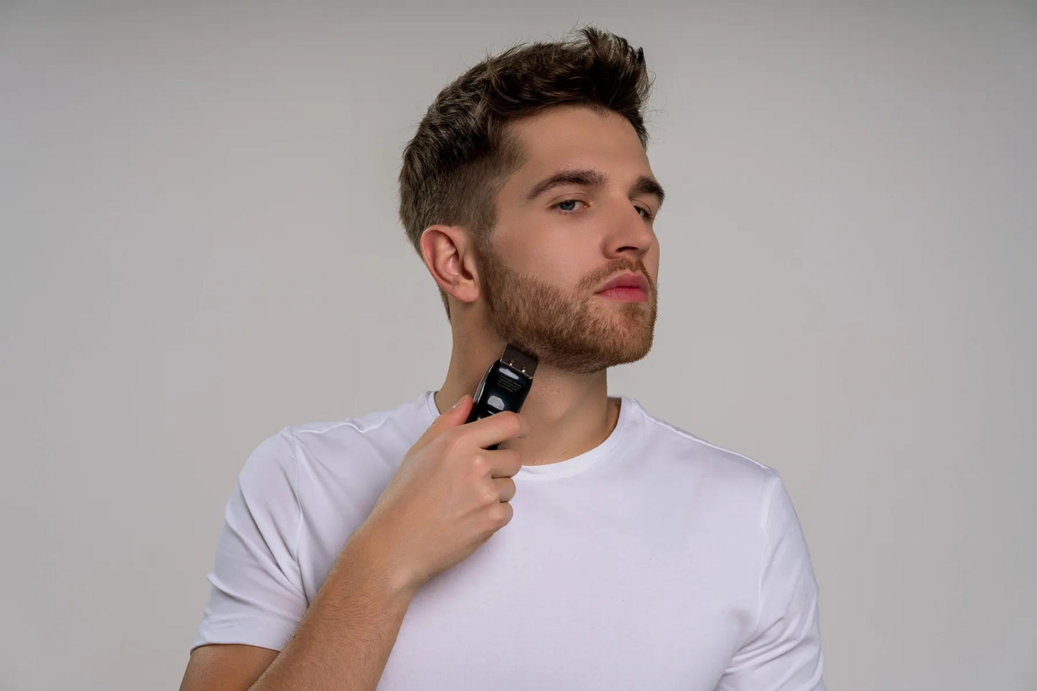 Ein Mann mit Bart trimmt seinen Hals mit einem elektrischen Trimmer.