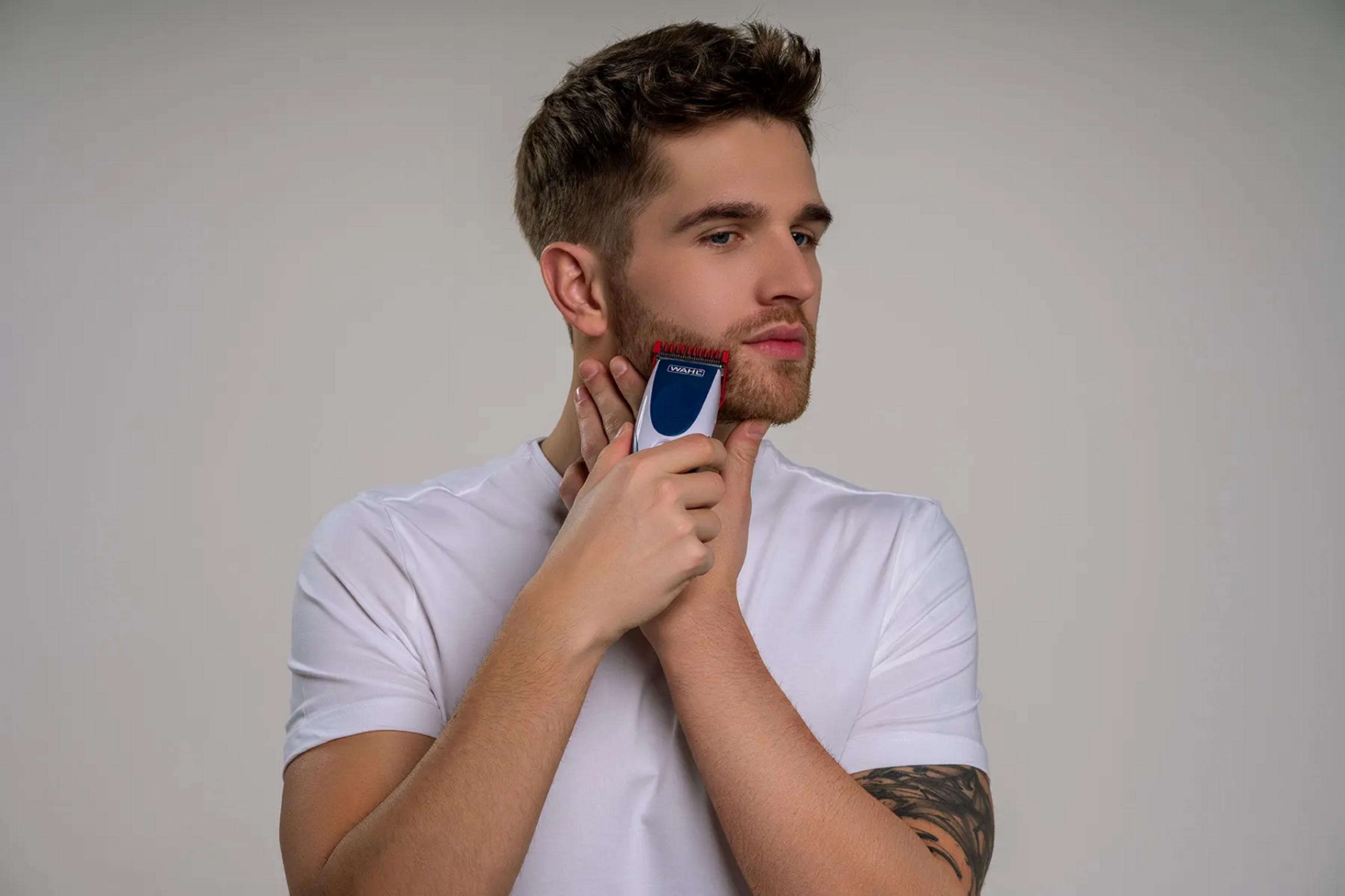 Ein Mann mit Bart trimmt sich mit einem blauen und weißen Trimmer.