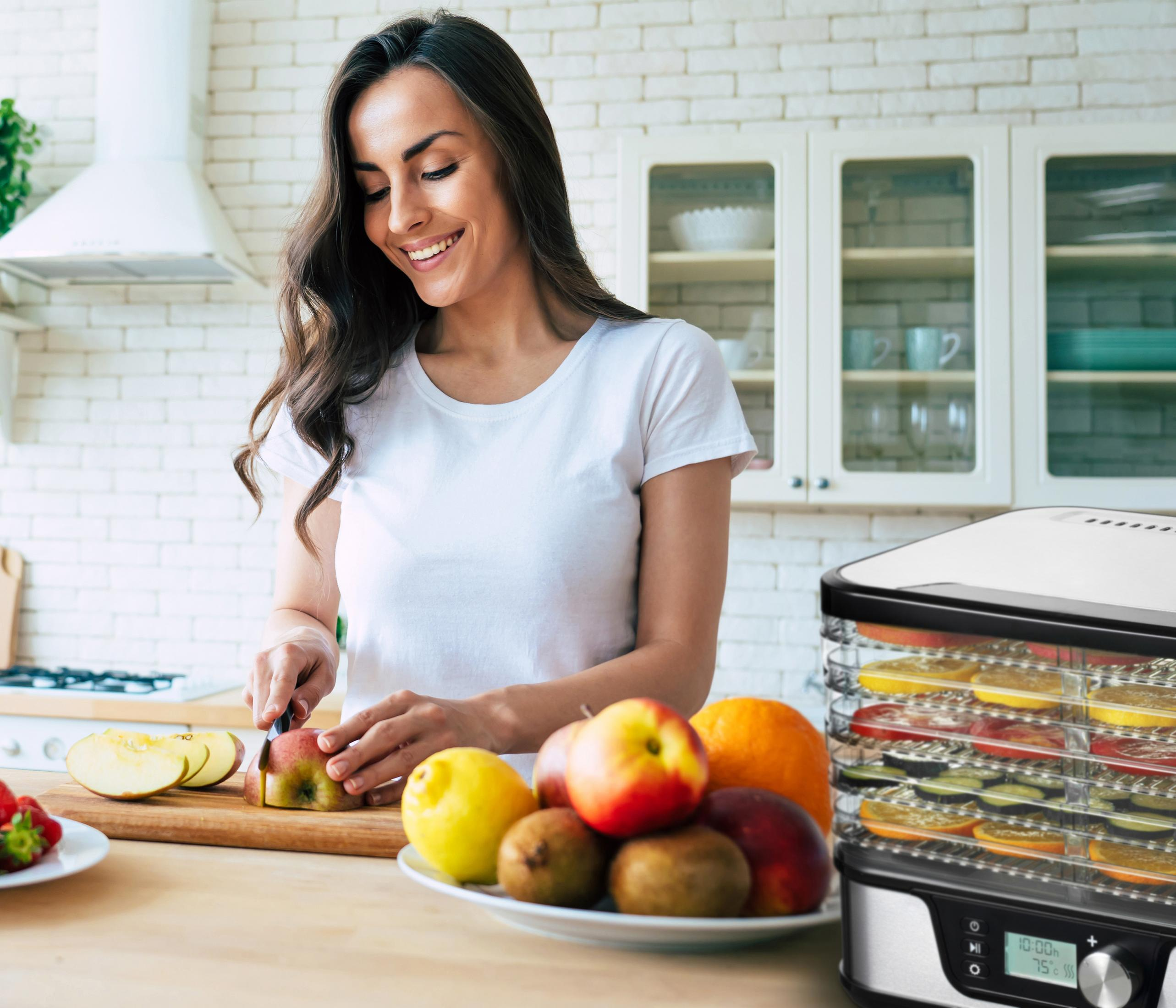 Femme coupant une pomme dans une cuisine, déshydrateur avec fruits et légumes devant.