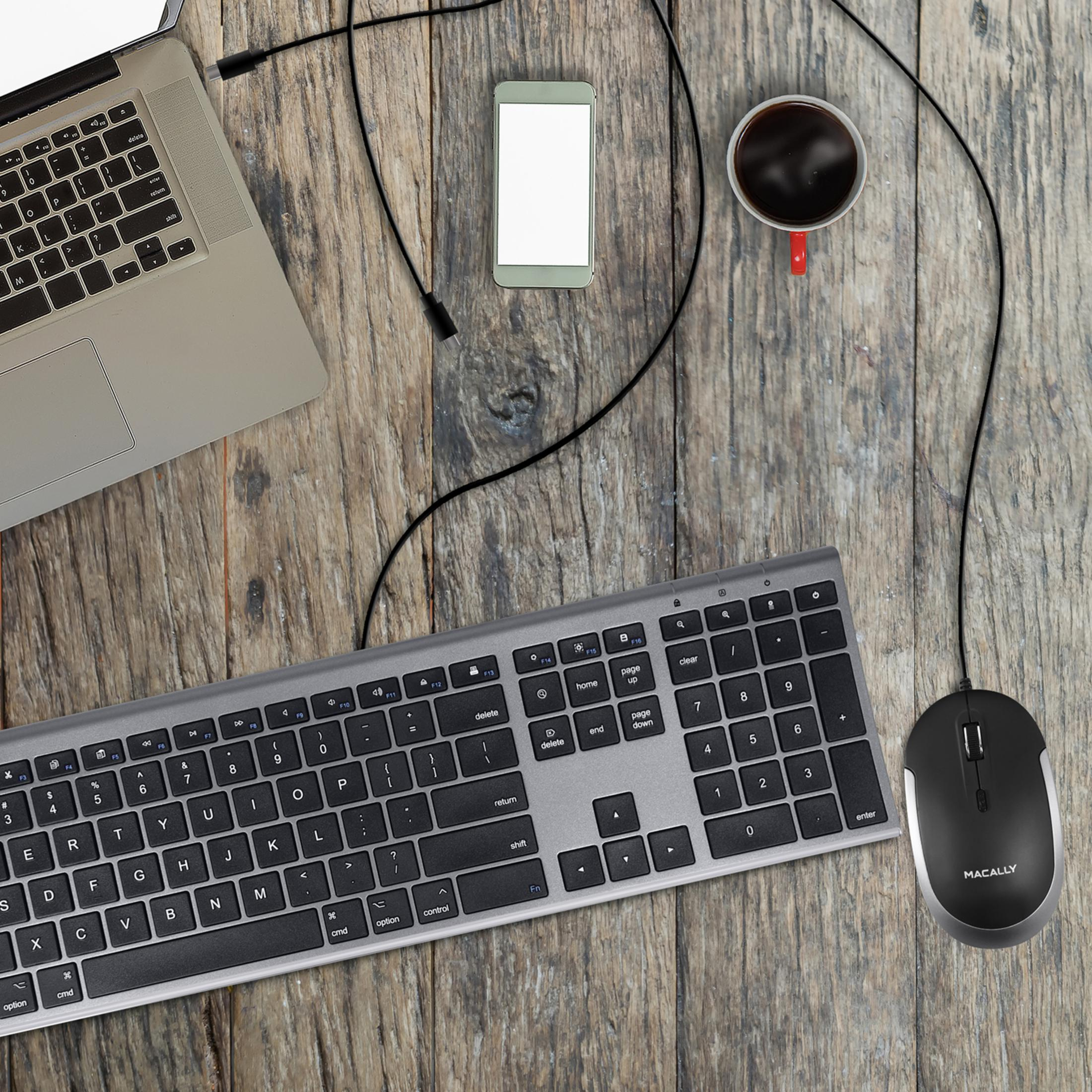 Portátil, teclado, ratón, smartphone y taza de café sobre mesa de madera.