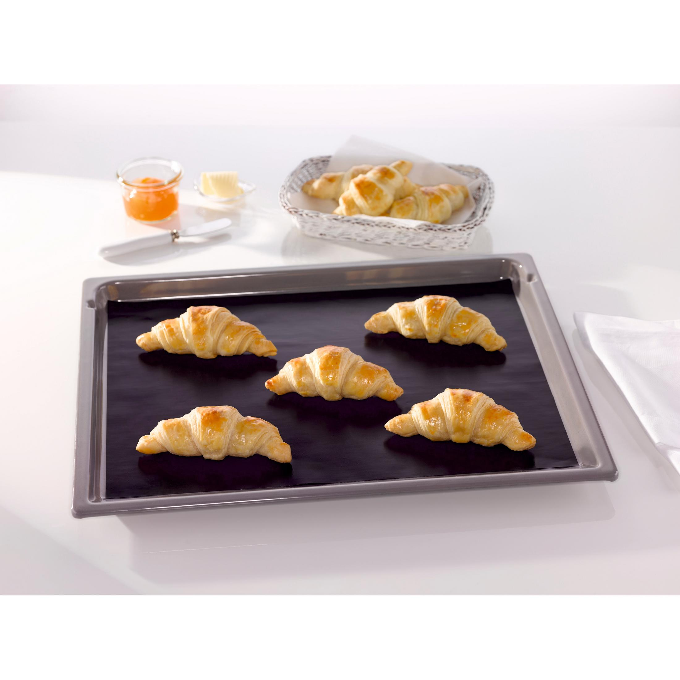 Fünf goldene Croissants auf einem schwarzen Backblech mit Marmelade und Butter im Hintergrund.