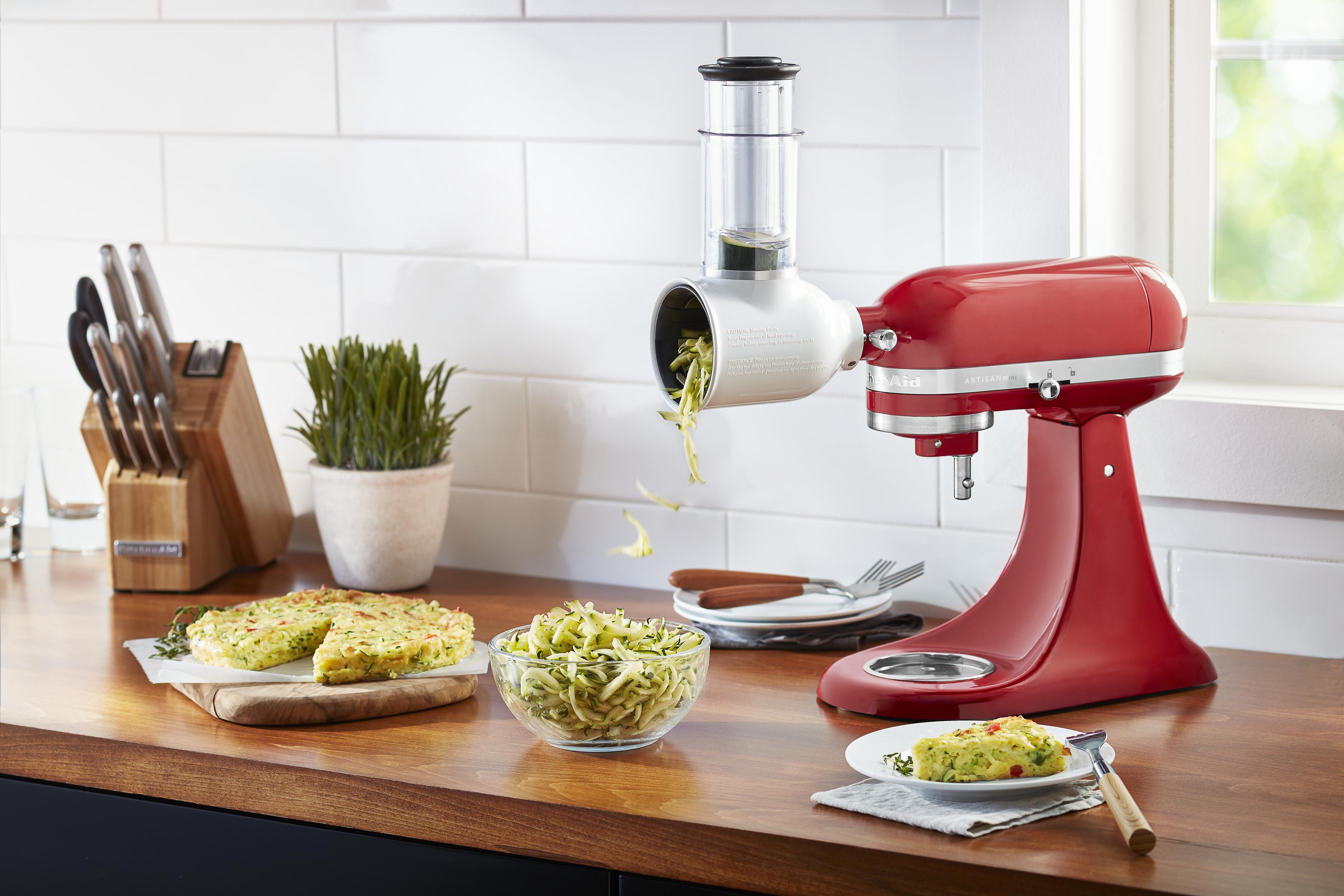 Kırmızı bir KitchenAid stand mikseri ve kabak rendesi aparatı. Kabak şeritleri dökülüyor.