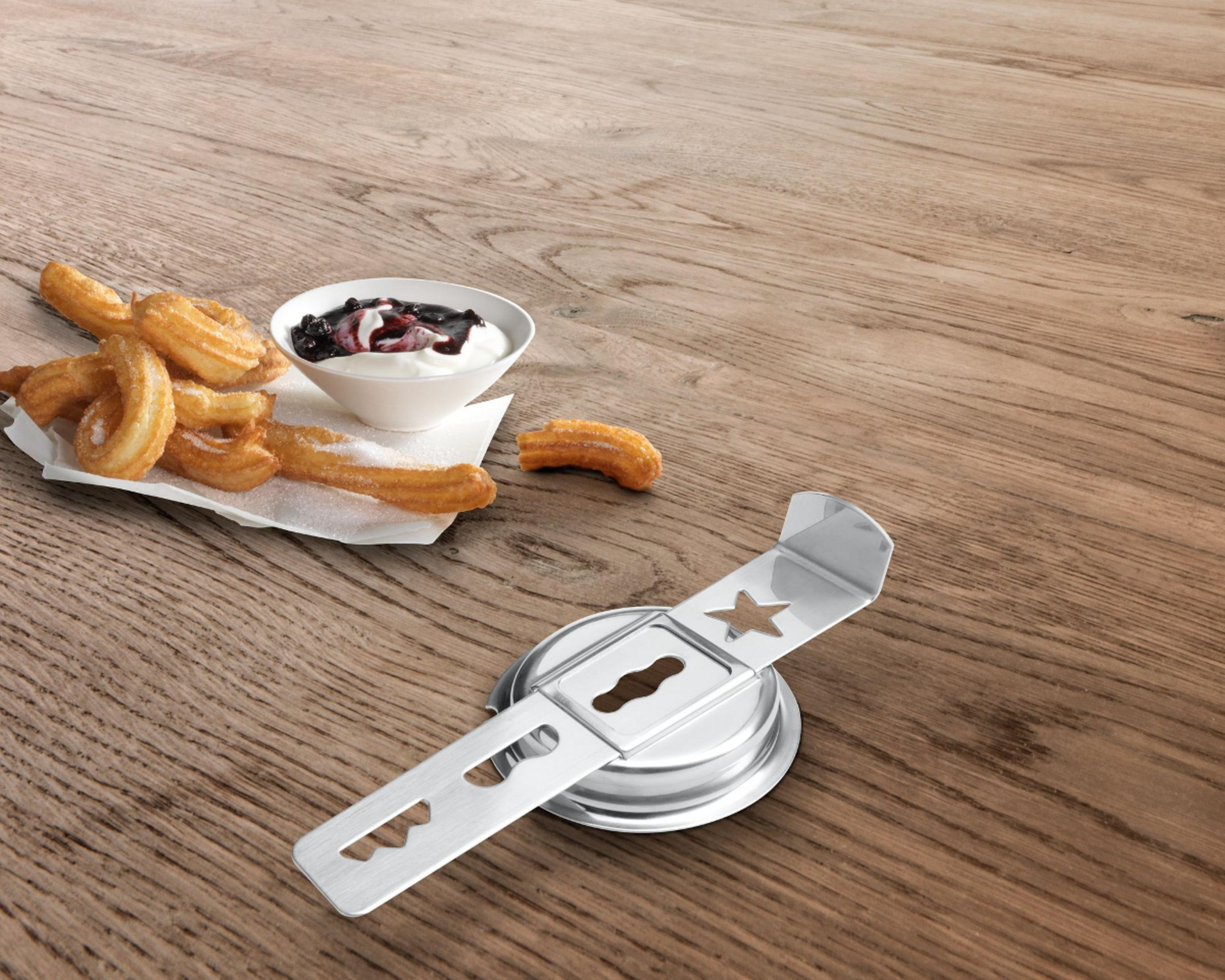 Churros mit Puderzucker, Joghurt mit Beeren und ein Metallwerkzeug liegen auf einem Holztisch.